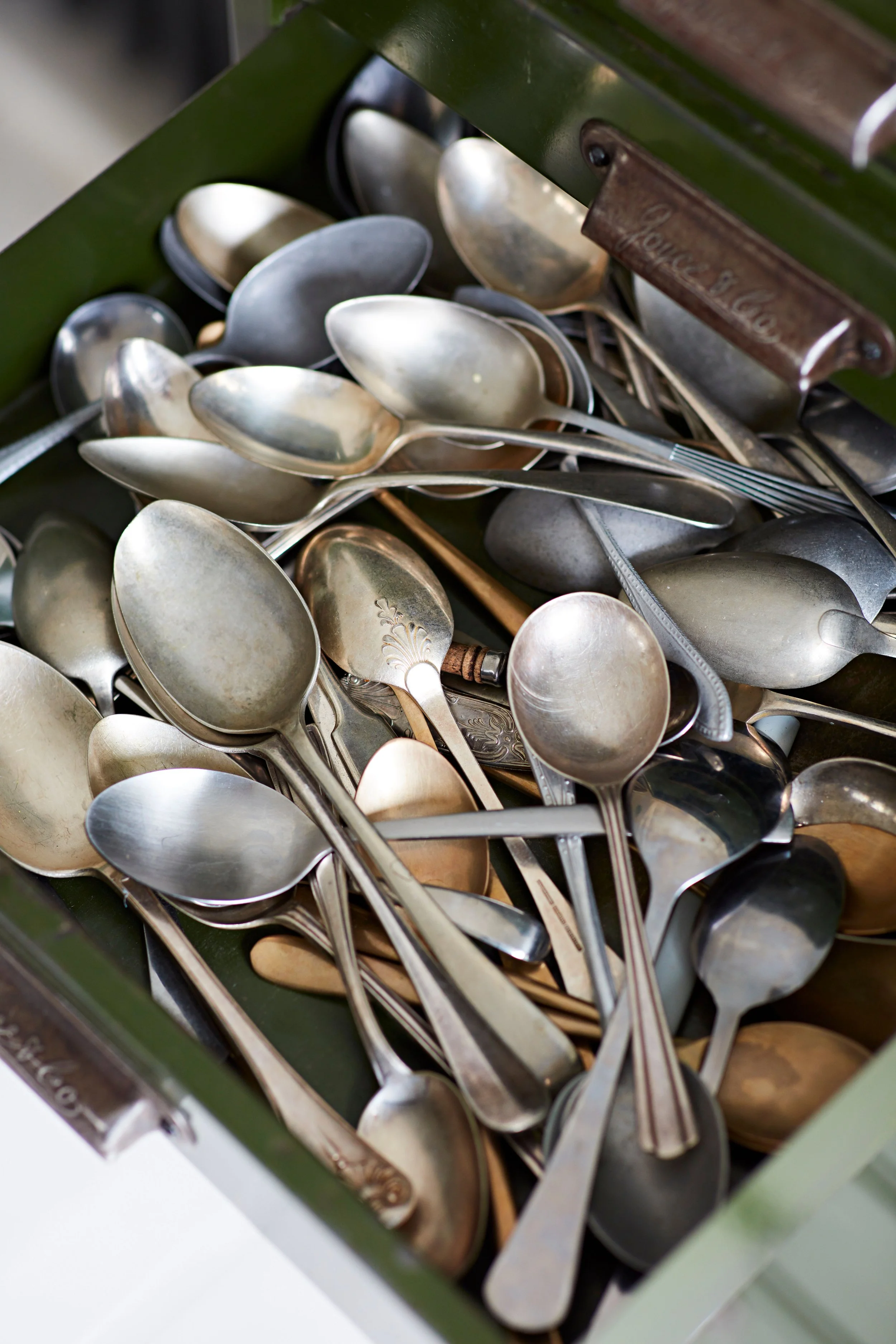 A collection of silver and metal spoons in a green drawer.
