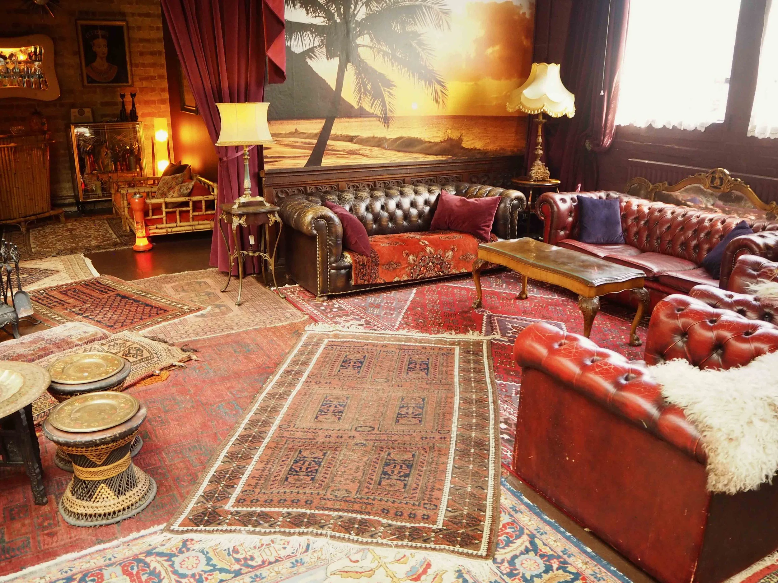 Living room with vintage furniture, including leather sofas, traditional rugs, and a sunset beach mural on the wall.