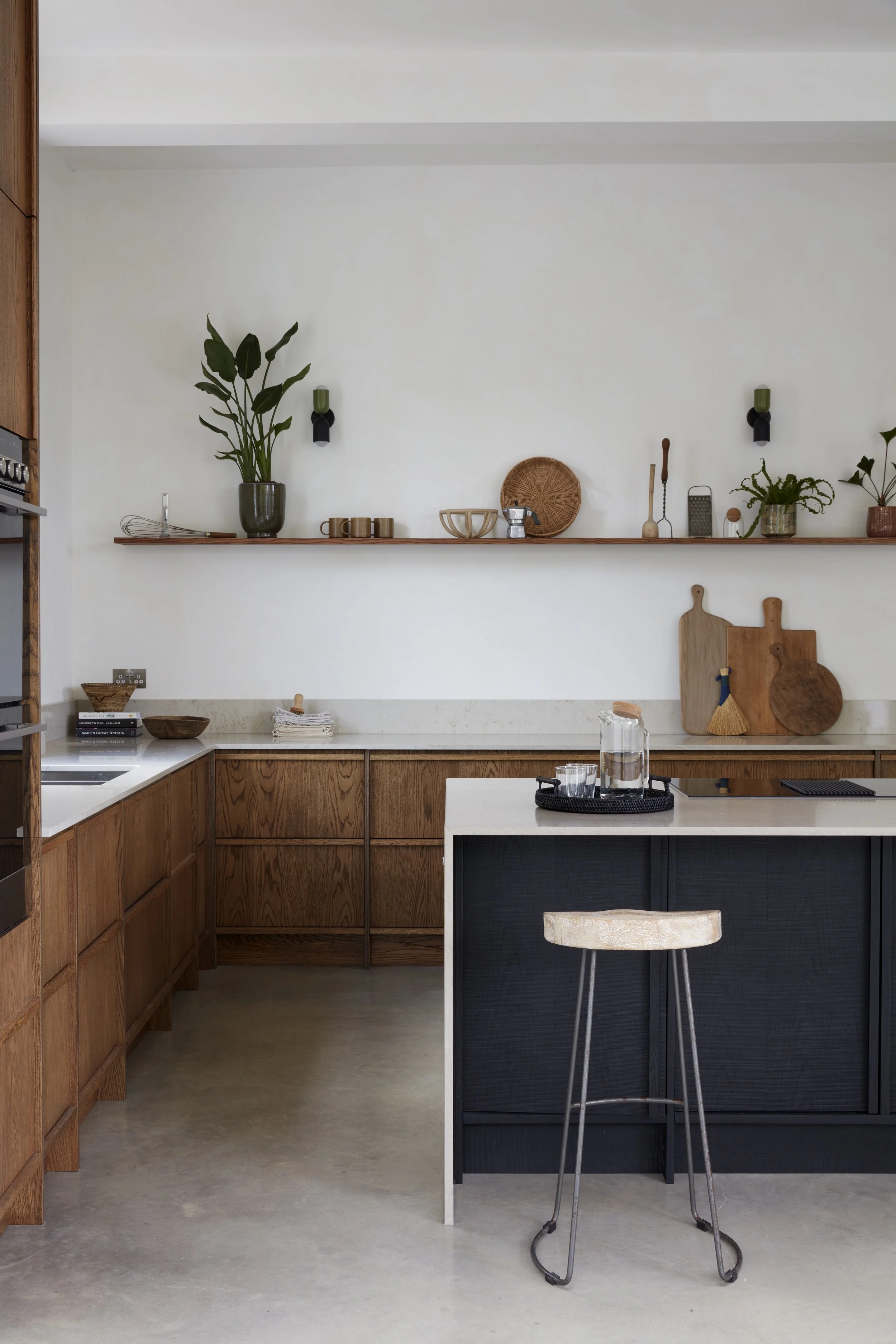 Modern kitchen with wooden cabinets, white countertops, a black island, and decorative shelves with plants and kitchenware.