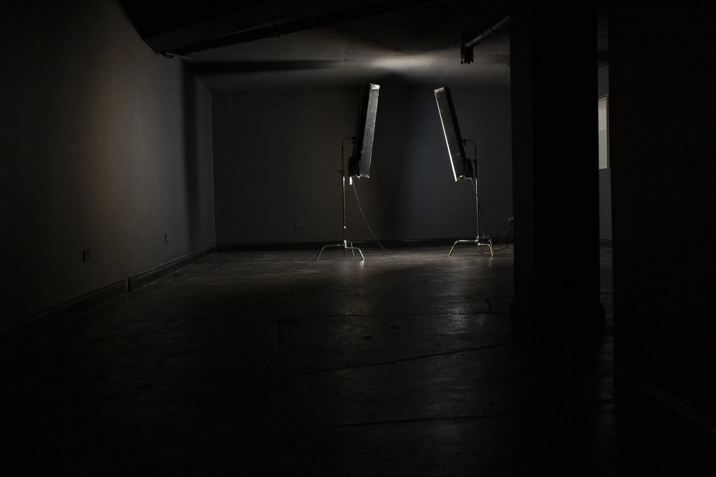 Dimly lit room with two large studio lights on stands facing each other against a dark wall.