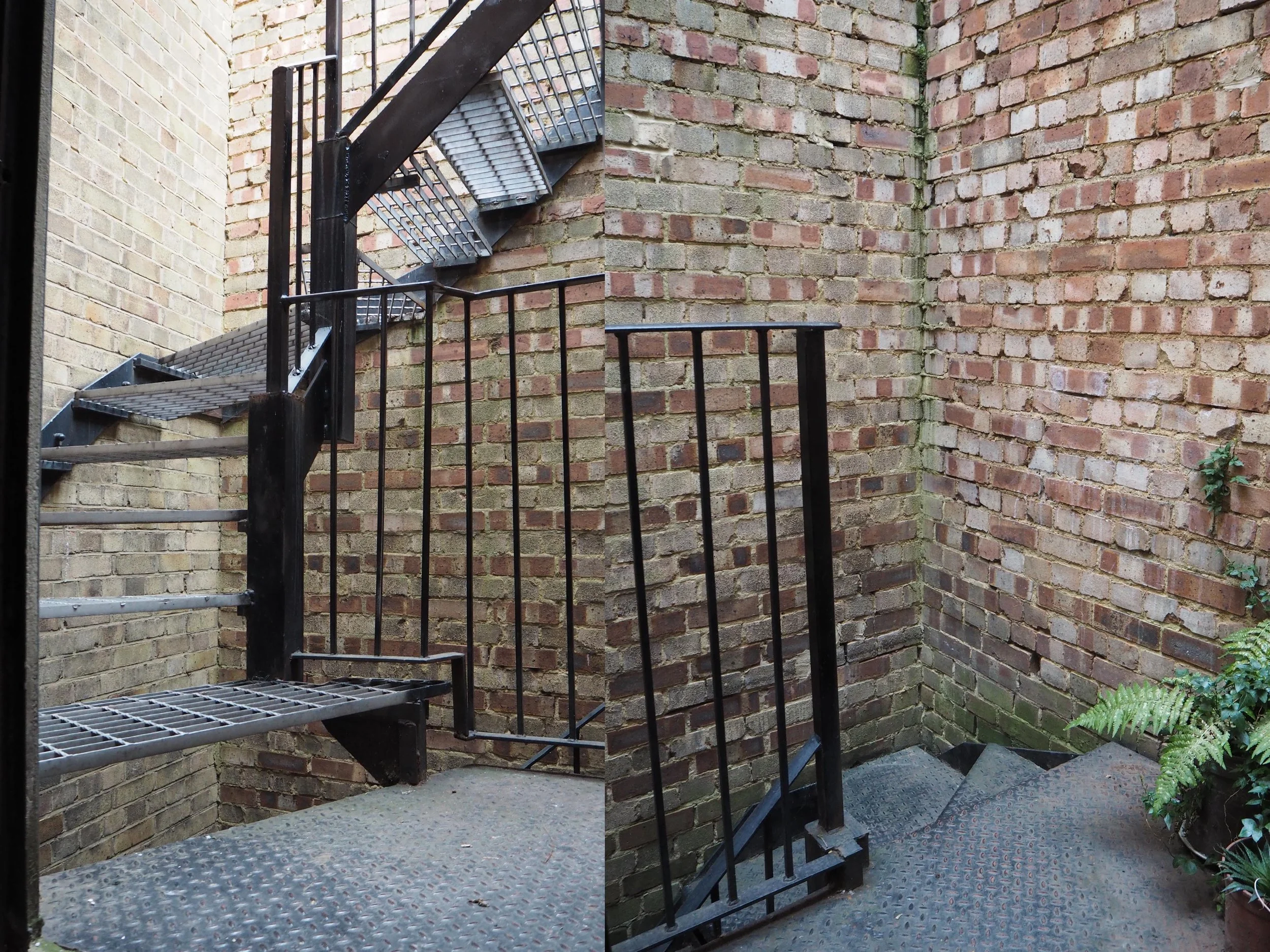 An outdoor fire escape staircase made of metal with black railing, attached to an aged brick wall in an alleyway. The staircase has several steps and a small landing at the bottom with a potted plant on the right side.