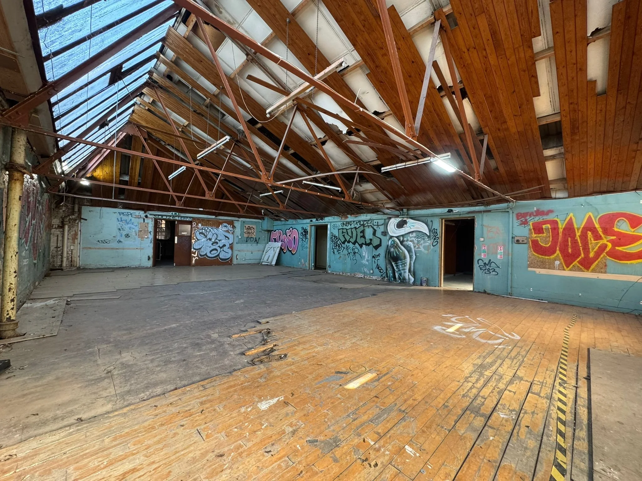 Abandoned building with a damaged roof, graffiti on blue walls, and a peeling wooden floor.