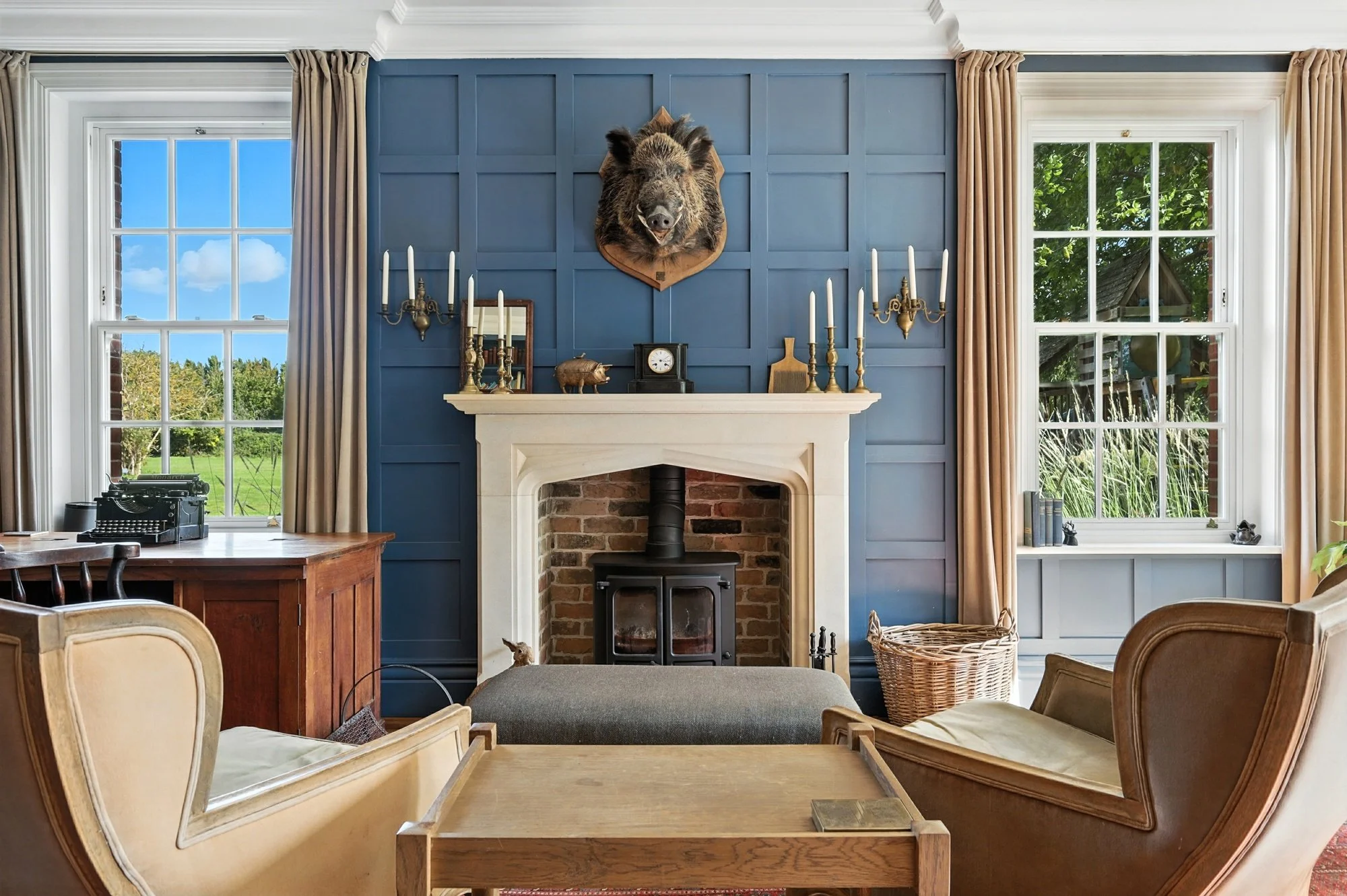 Living room with blue accent wall and a television mount shaped like a boar's head, surrounded by windows with beige curtains, a fireplace, and various decorative items.