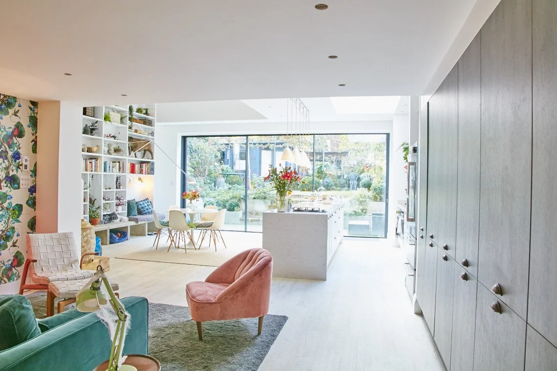 Bright, modern open-concept living and dining area with large glass doors opening to a lush outdoor garden.