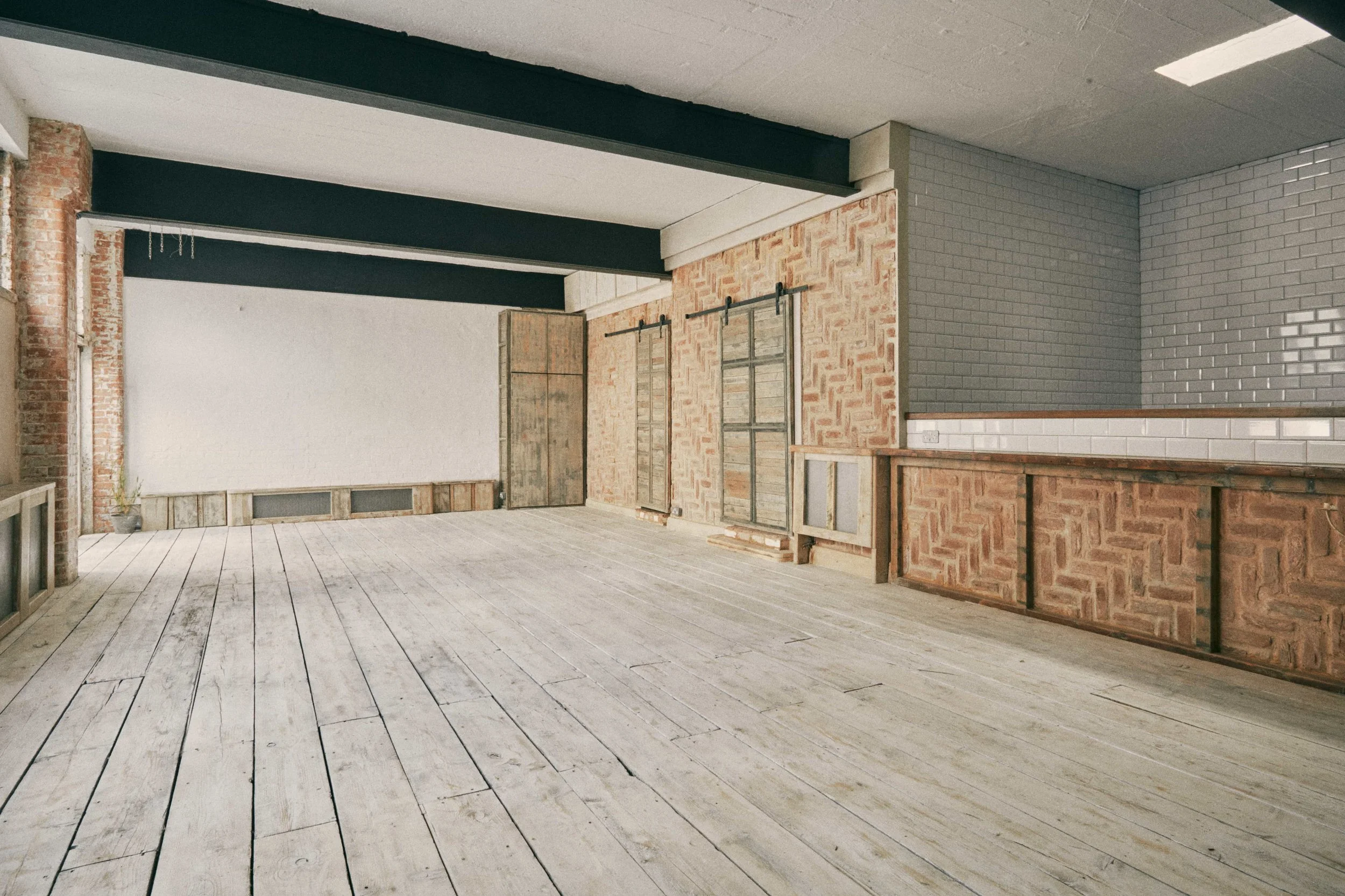 An interior space with exposed brick walls, white and gray tiles, sliding barn doors, and a wooden floor.