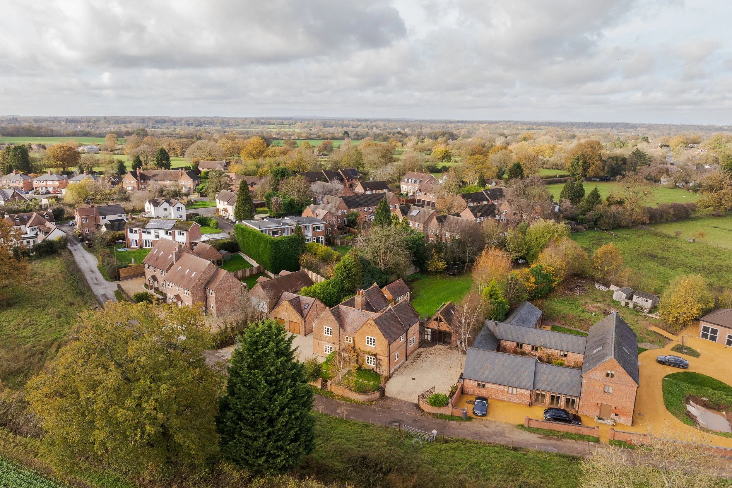 Aerial view of a suburban neighborhood with houses, trees, and green fields under cloudy sky