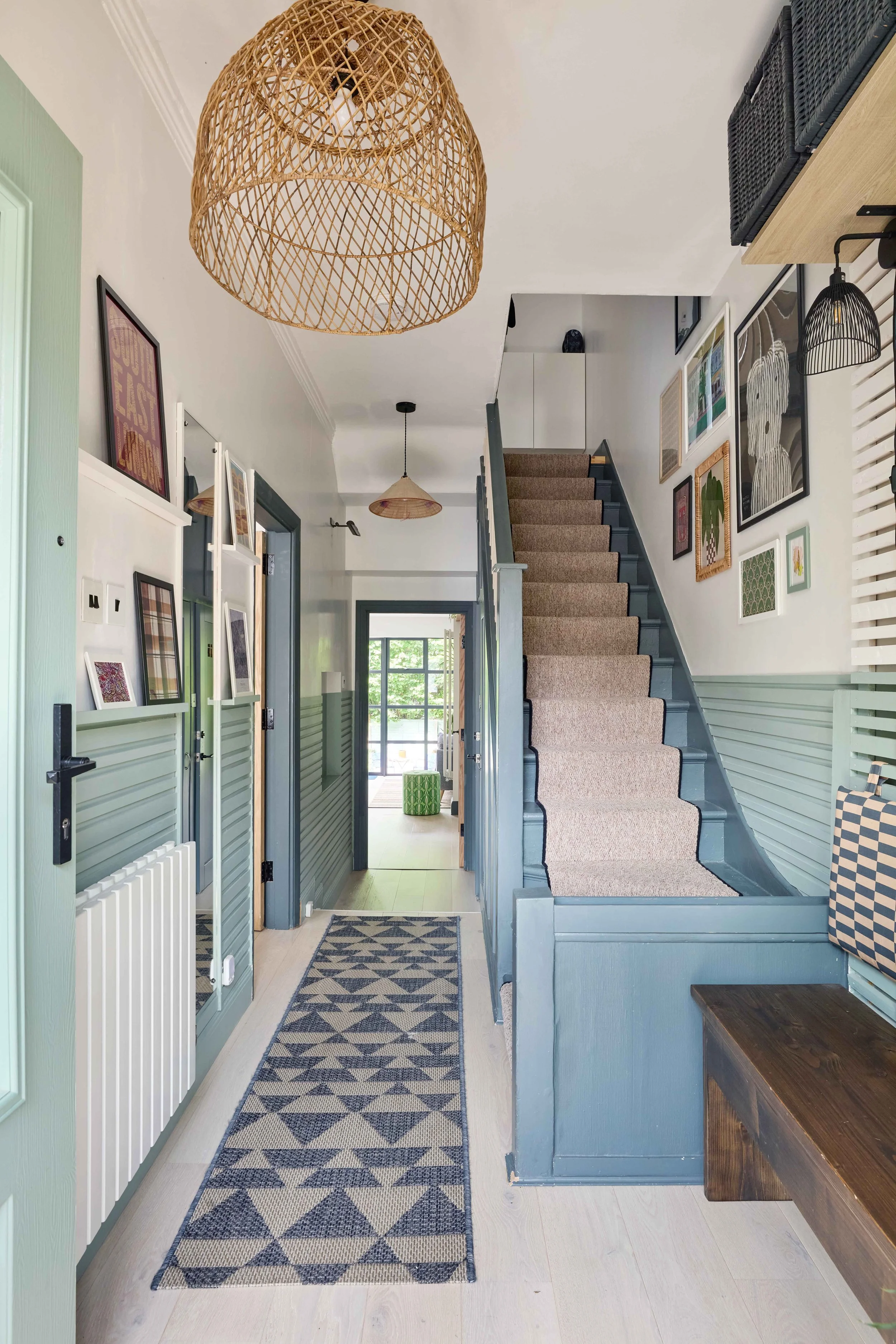 Interior view of a hallway with a staircase, wall art, woven light fixtures, a rug, and a bench.