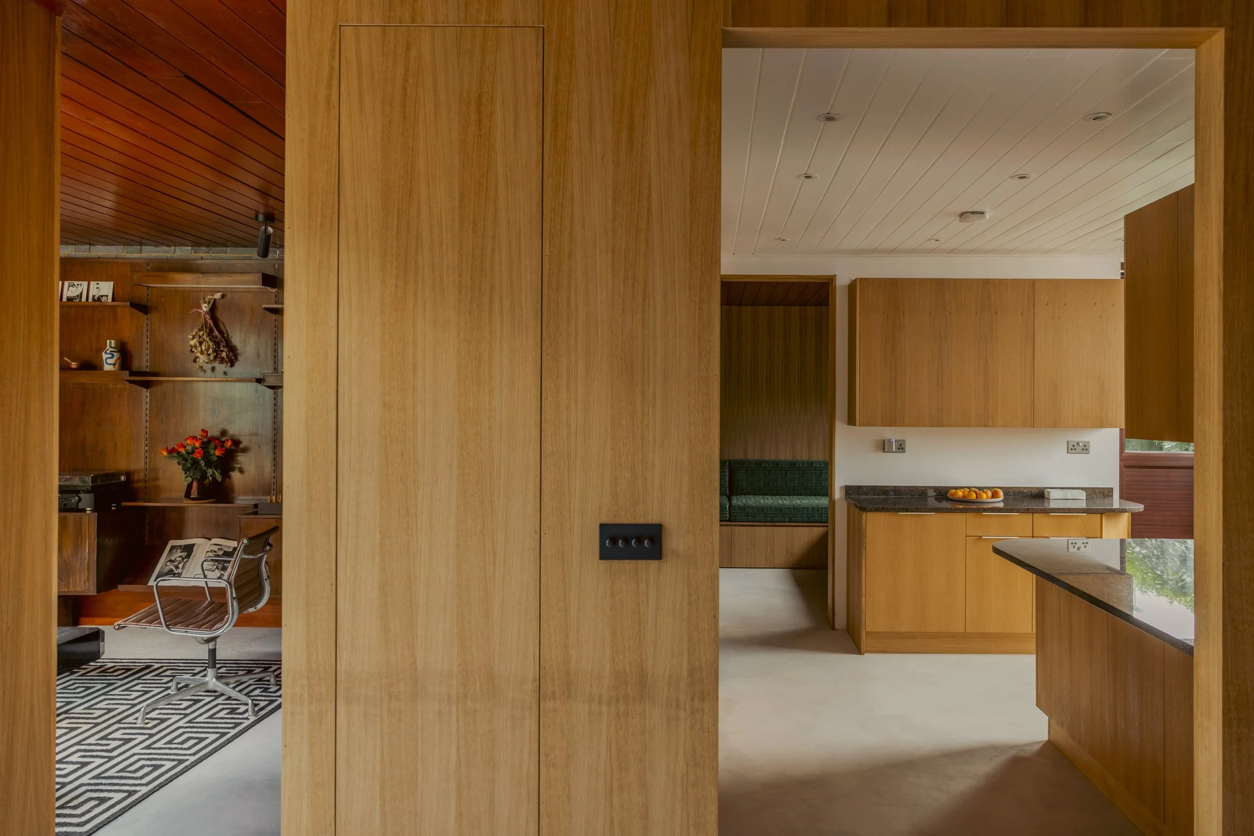 Interior view of a wooden kitchen and office space with a modern design, wood cabinetry, and a seating nook with green upholstery.
