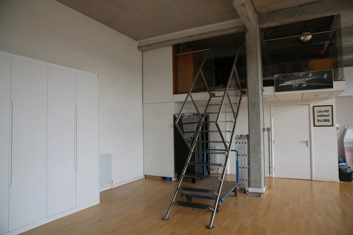 Interior room with a metal staircase leading to a loft, white walls, wooden floor, and various storage cabinets and closet doors.
