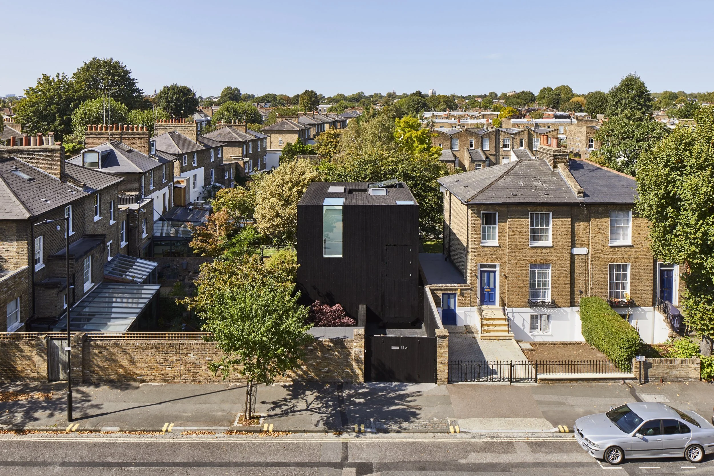 Cityscape showing rows of brick houses with streets, trees, and a blue sky.