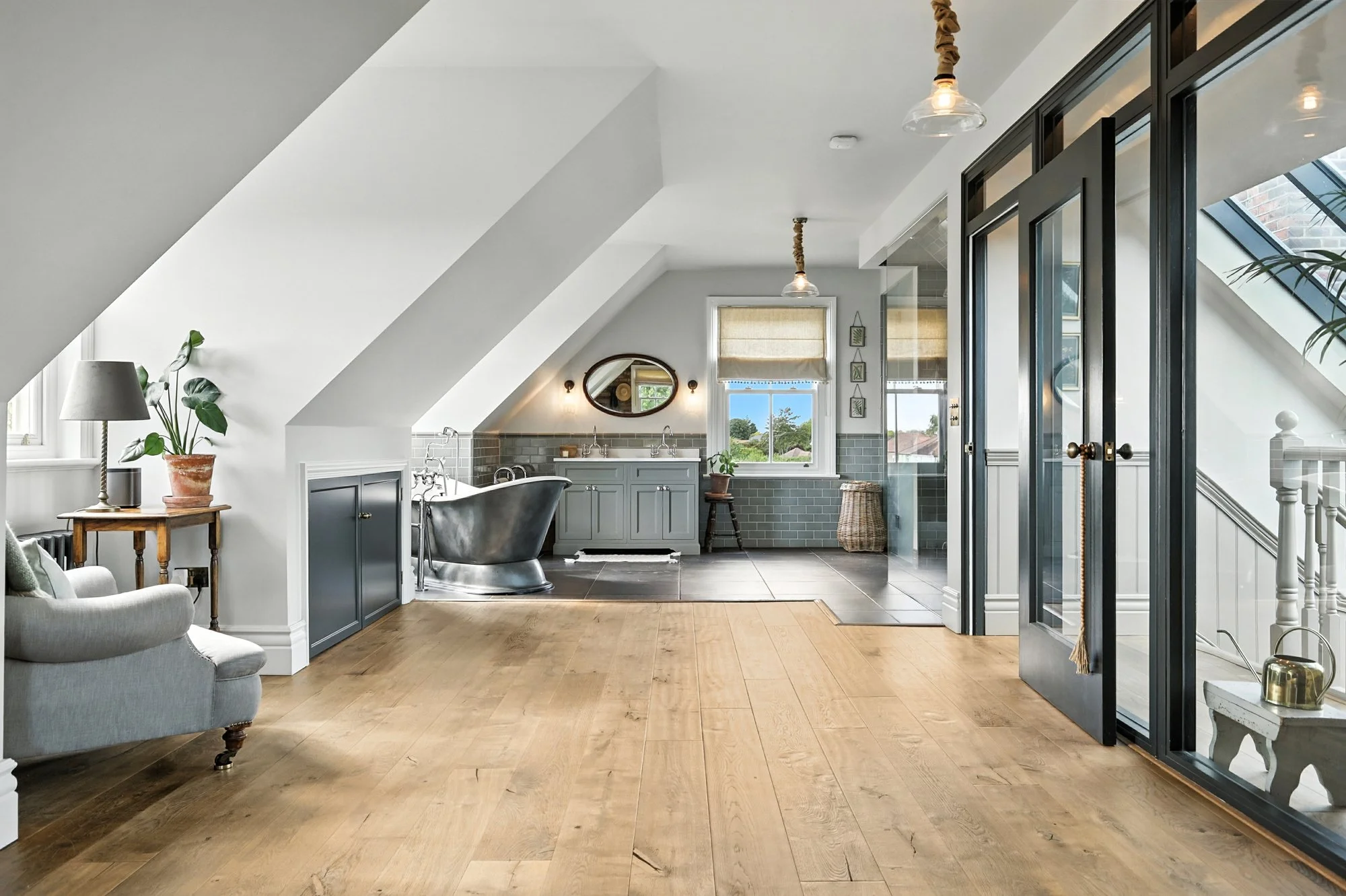 Modern attic bathroom with a vintage freestanding bathtub, vanity with two sinks, and large windows letting in natural light.