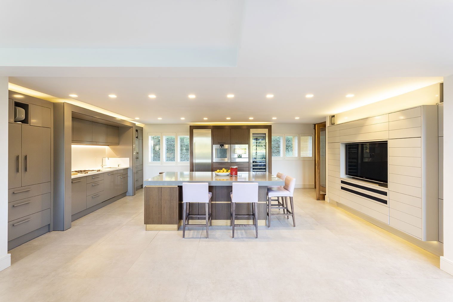 Modern kitchen with gray cabinets, a large island with seating, built-in appliances, and a wall-mounted TV.