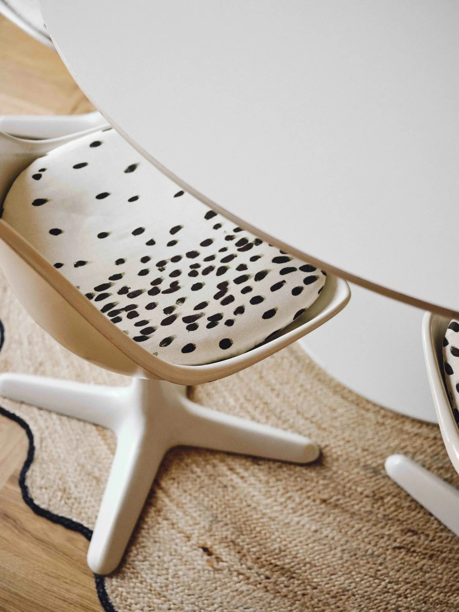 Close-up of a white chair with a cushioned seat featuring black polka dots, placed on a beige rug in a room with wooden flooring.