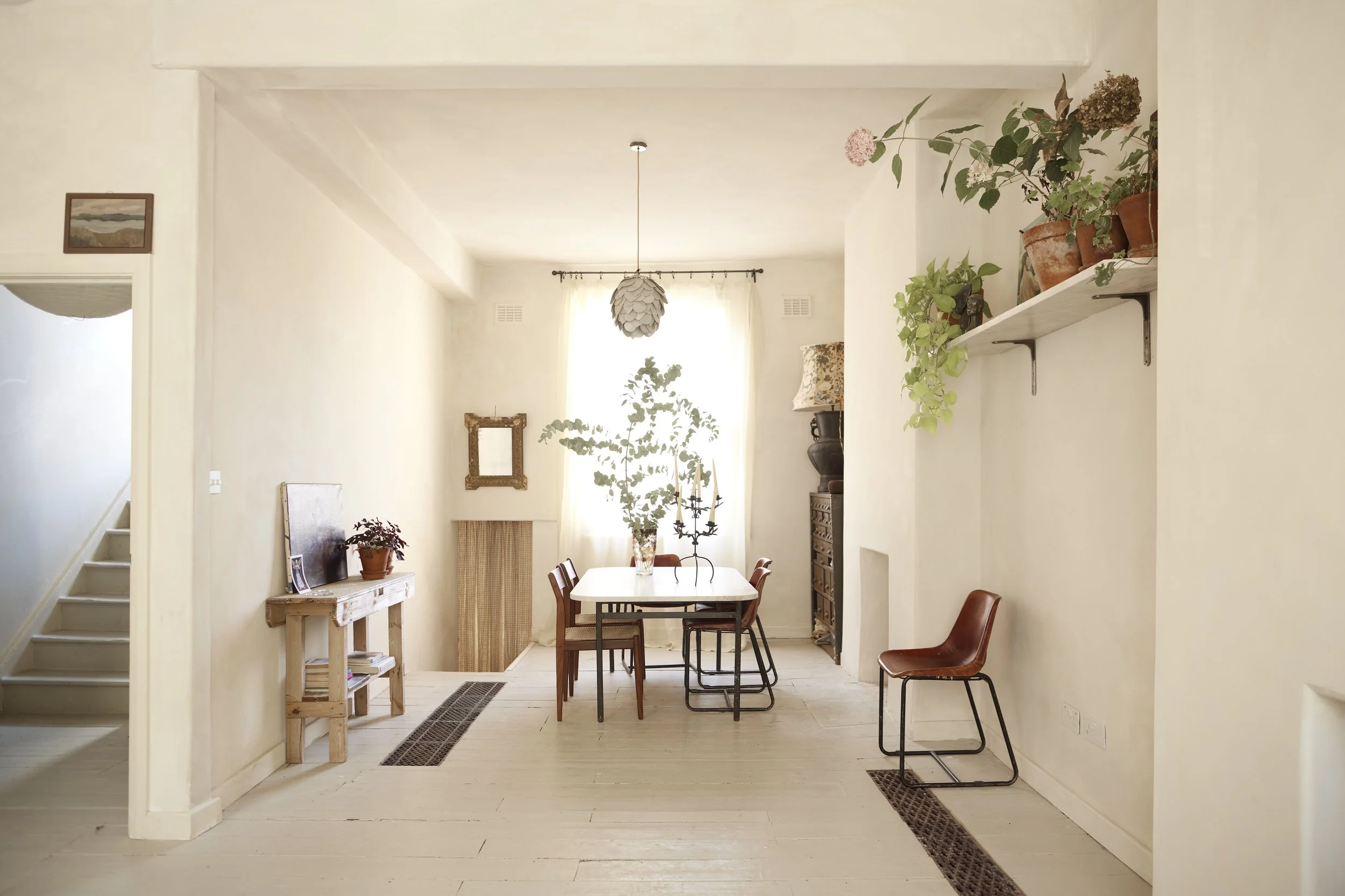 A dining room with a white table and chairs near a window, with potted plants and decorative items.