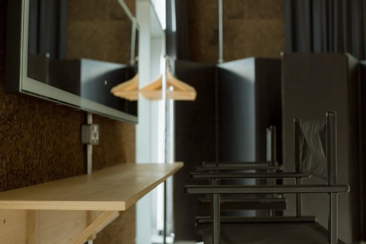 Empty black chairs with armrests are lined up against the wall in a modern interior space, with a mirror reflecting a coat hanger.