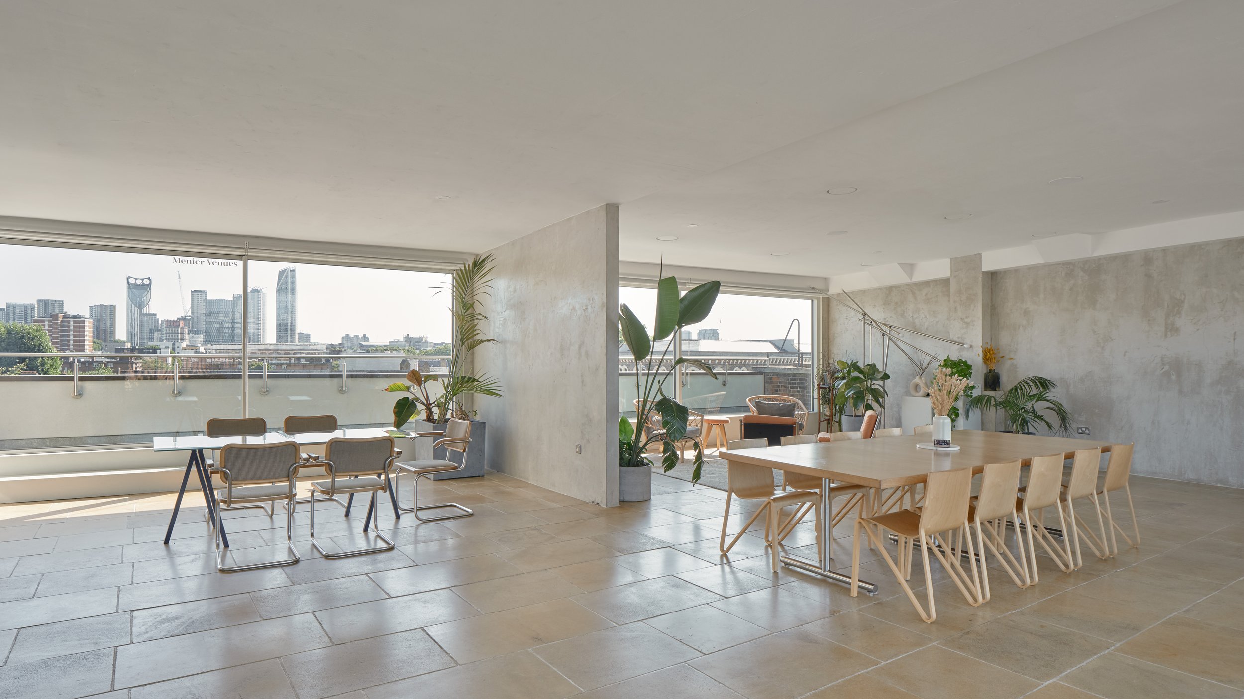 Modern, minimalist dining area with large windows overlooking a city skyline, wooden dining table surrounded by chairs, and various potted plants providing a natural touch.