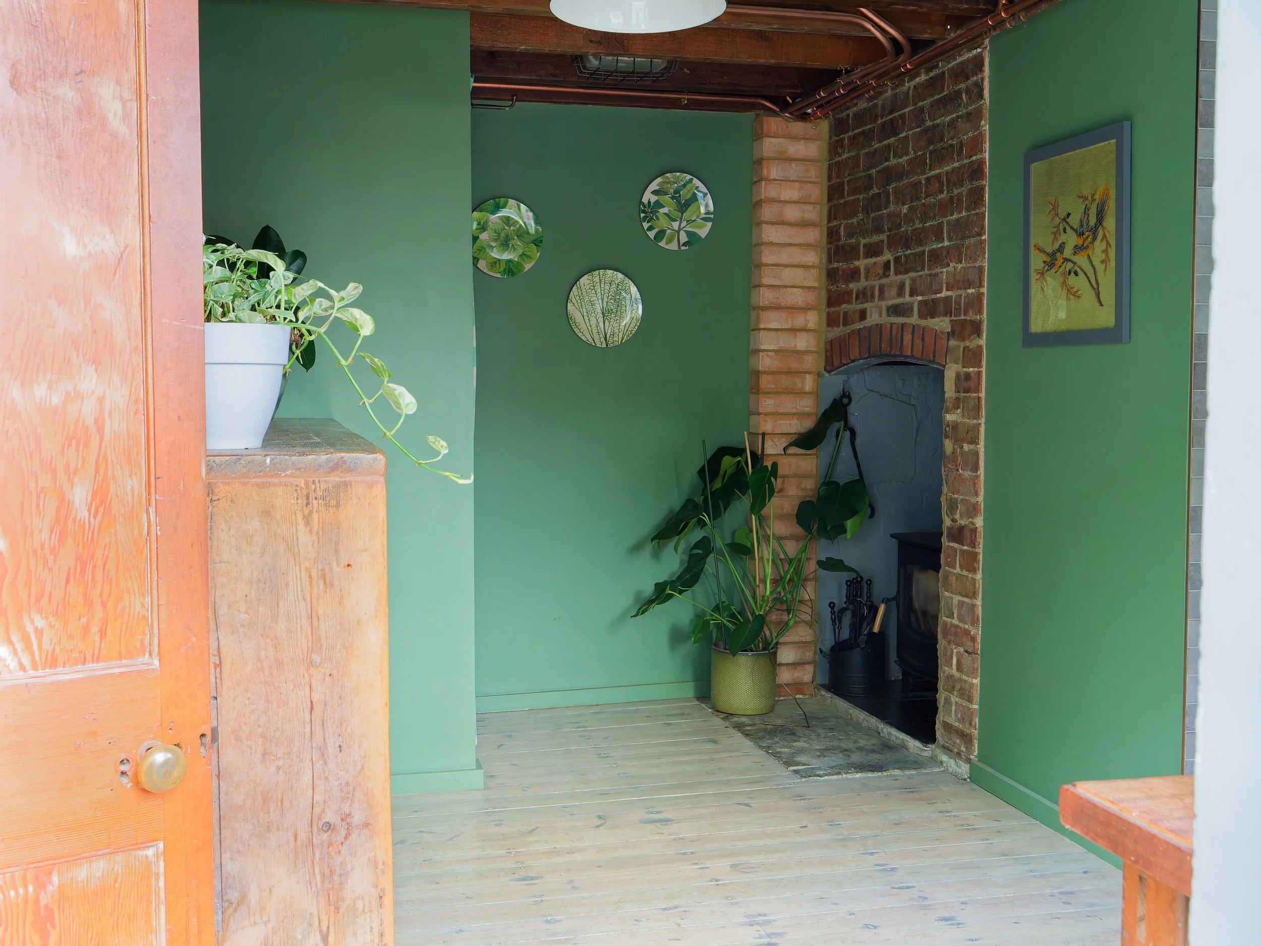 Interior of a room with green walls, a brick fireplace, potted plants, and decorative wall art.