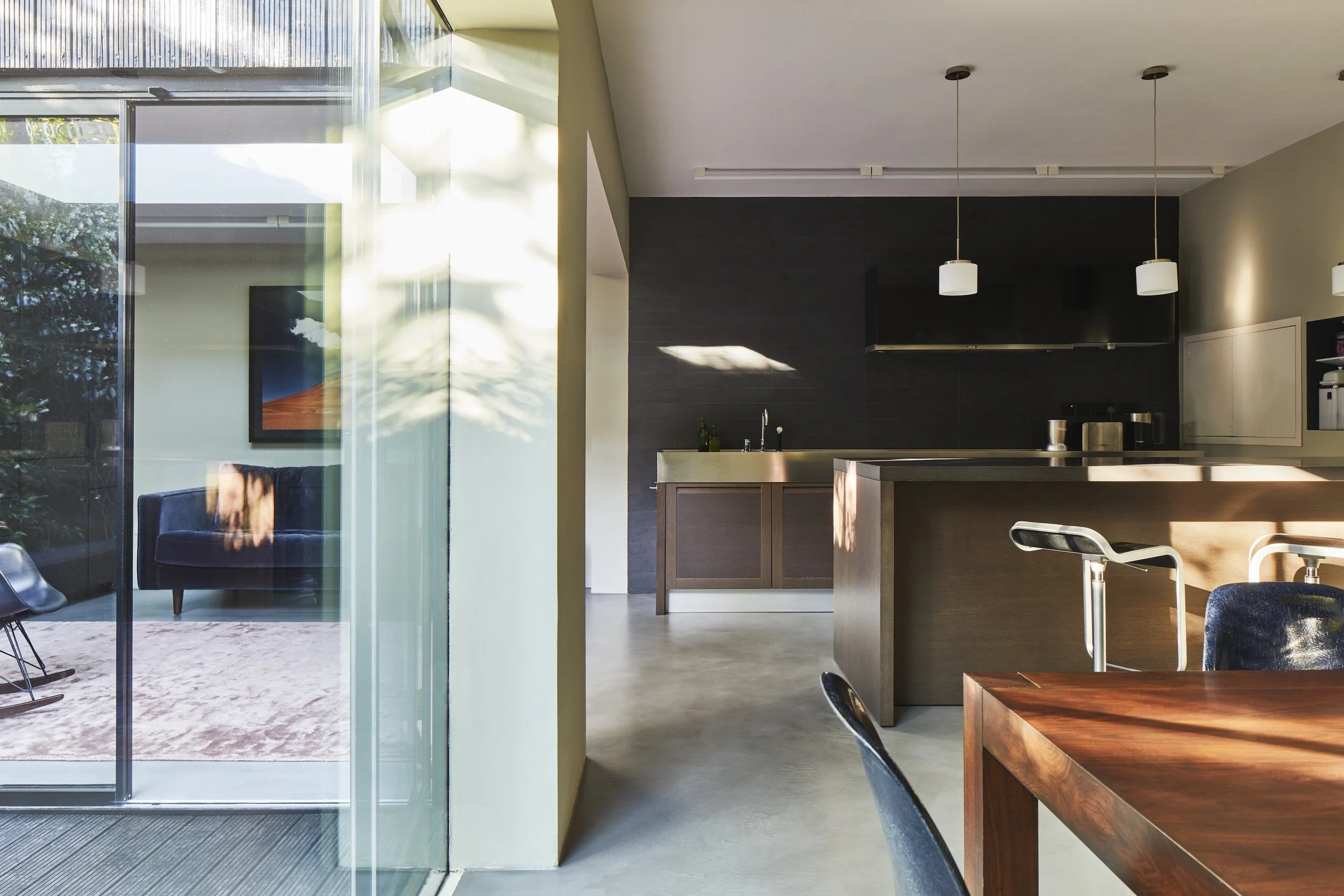 Modern kitchen and dining area with a sliding glass door leading to a living room with a black sofa and colorful artwork, natural light streaming in.