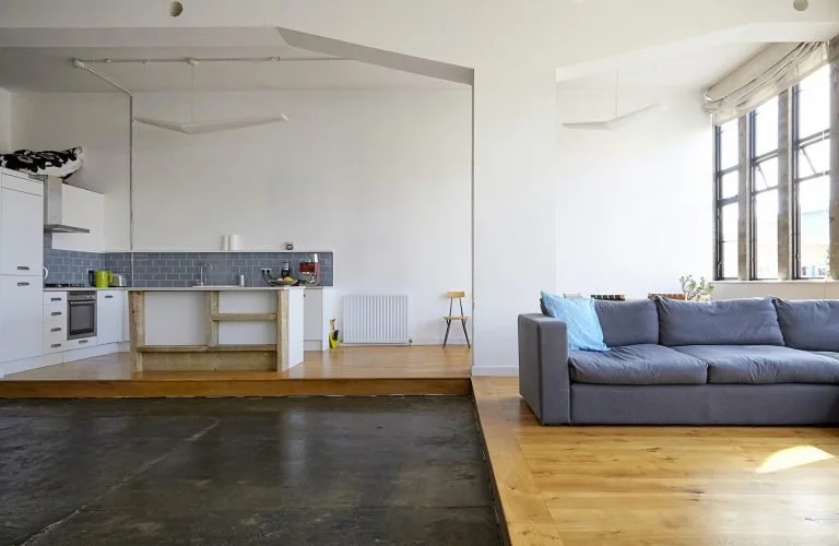 Open-concept living room and kitchen with a gray couch, large windows, and hardwood floors.