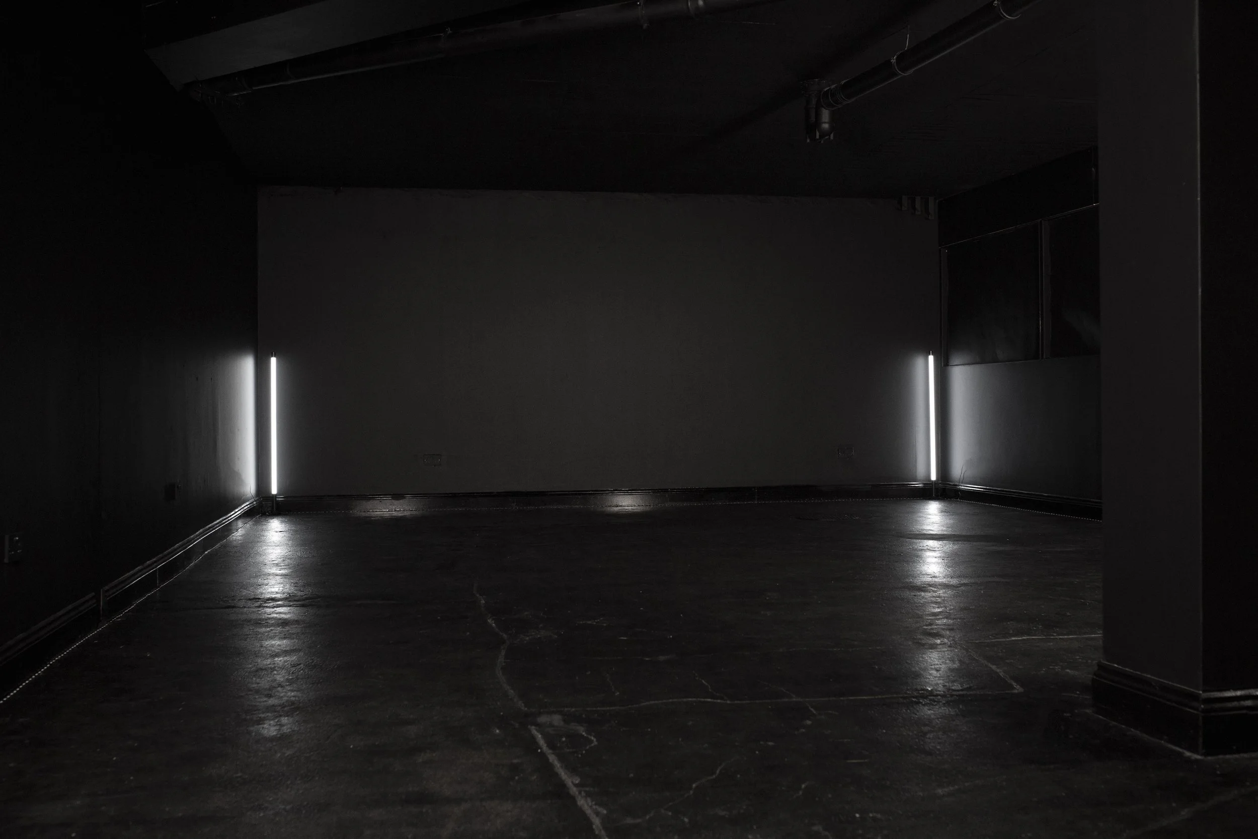 Dark, empty room with black walls and floor, illuminated by two vertical LED lights on either side of the back wall.