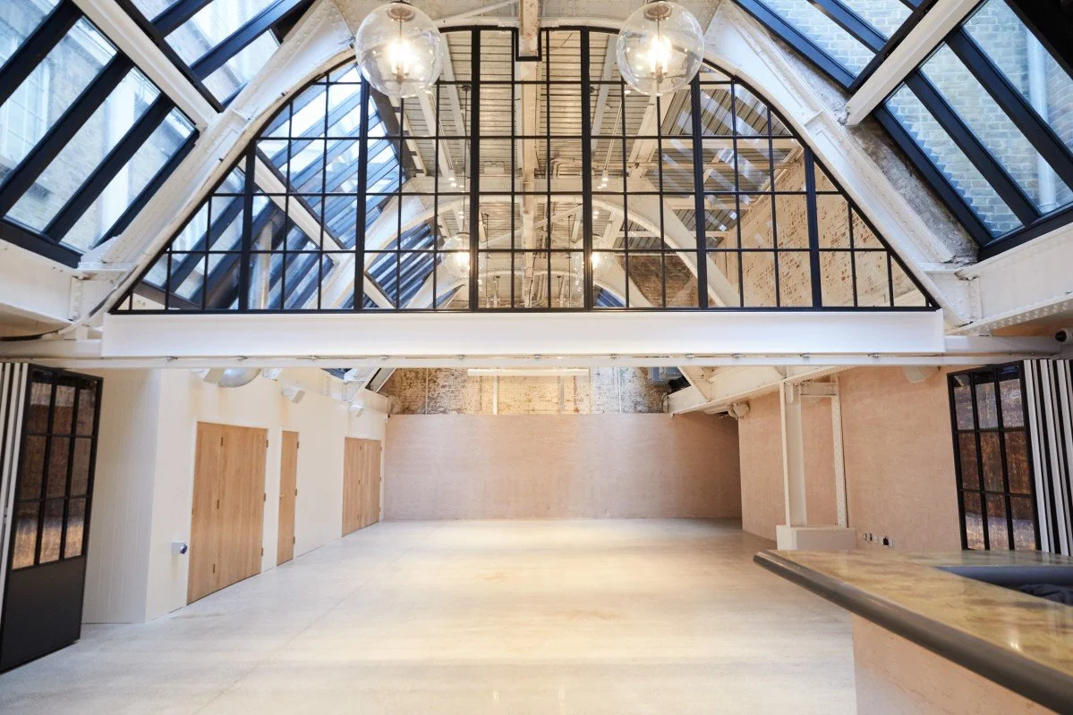 Empty interior space with large windows and glass ceiling, modern industrial style, light wooden doors, and a polished floor.