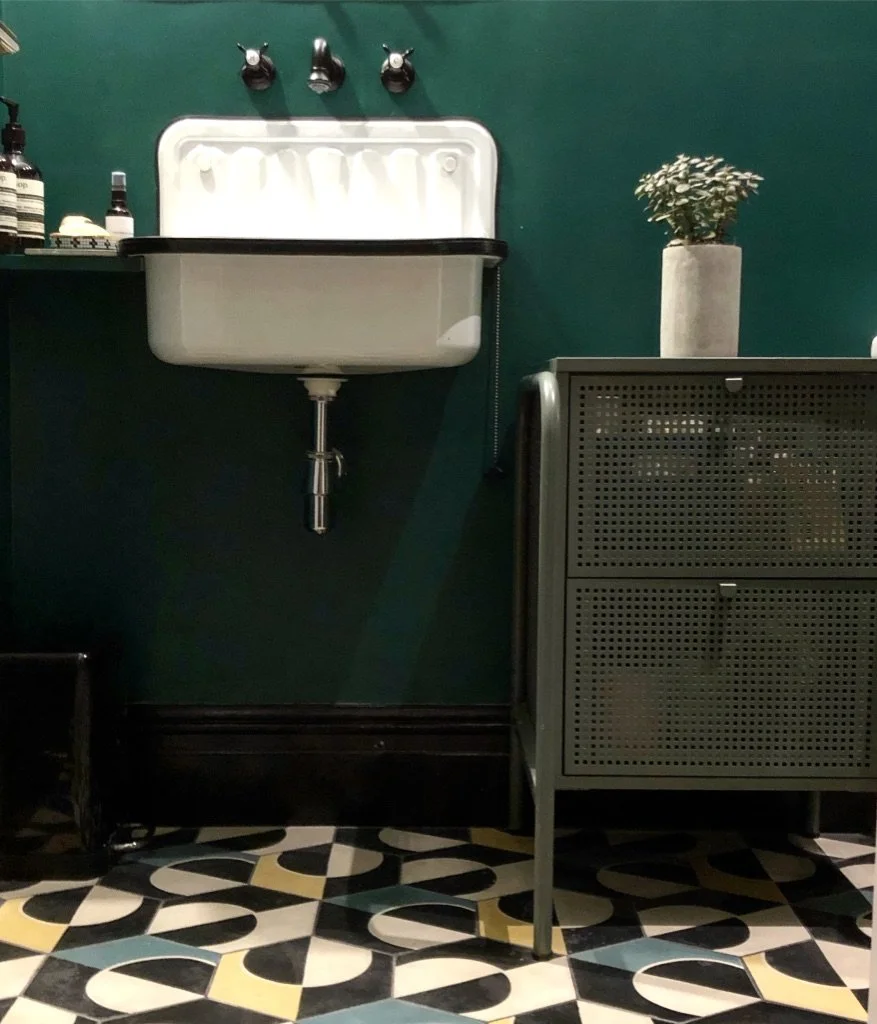 Bathroom with a vintage sink, a potted plant on a cabinet, and a decorative tile floor.