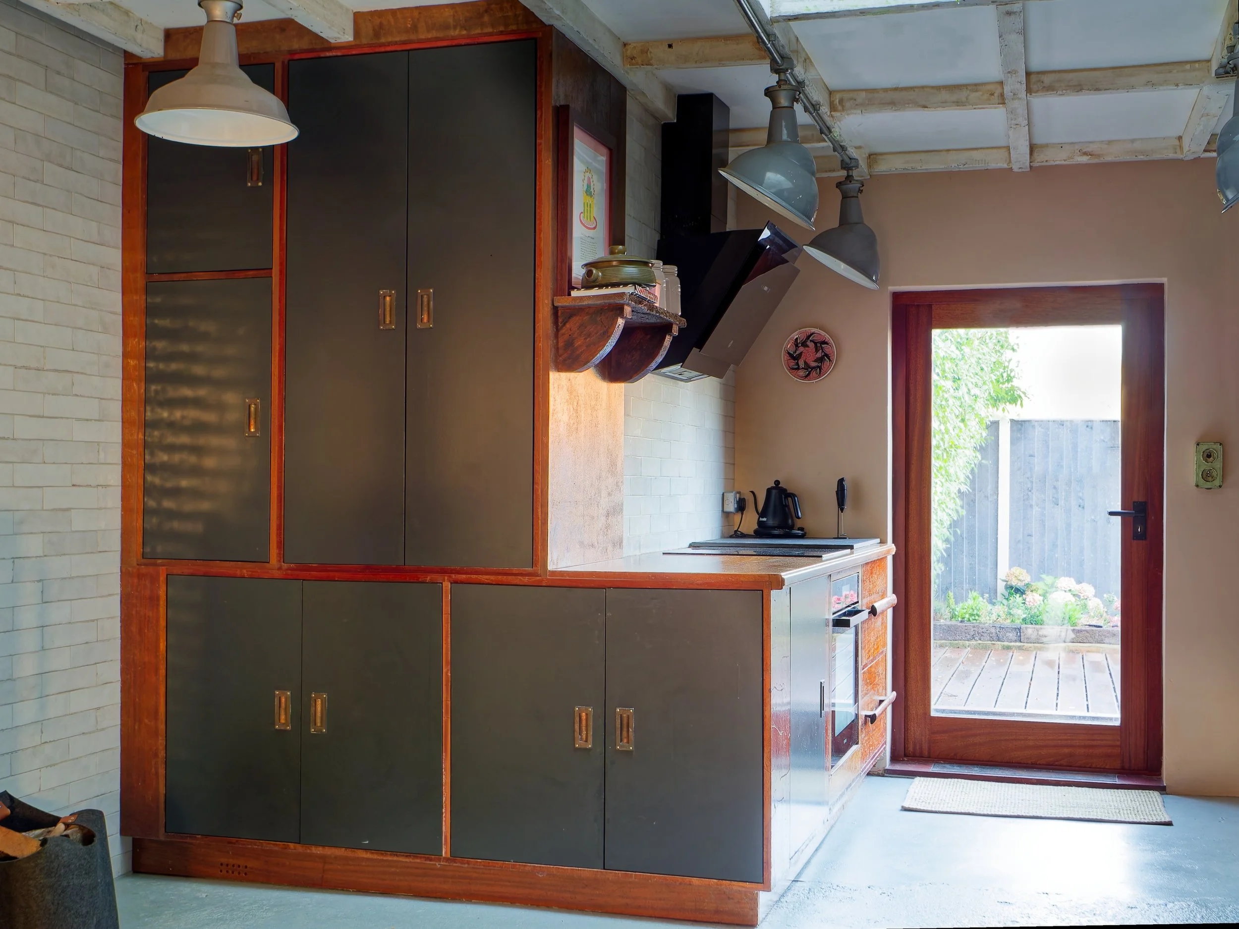 A cozy kitchen with a door leading outside, black and brown cabinets, hanging pendant lights, and a small wall decoration.