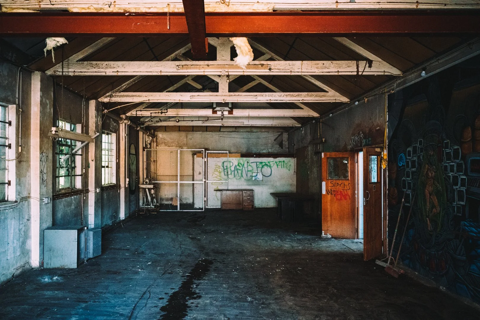 Interior of an abandoned industrial building with graffiti on the walls, broken windows, and dirt on the floor.