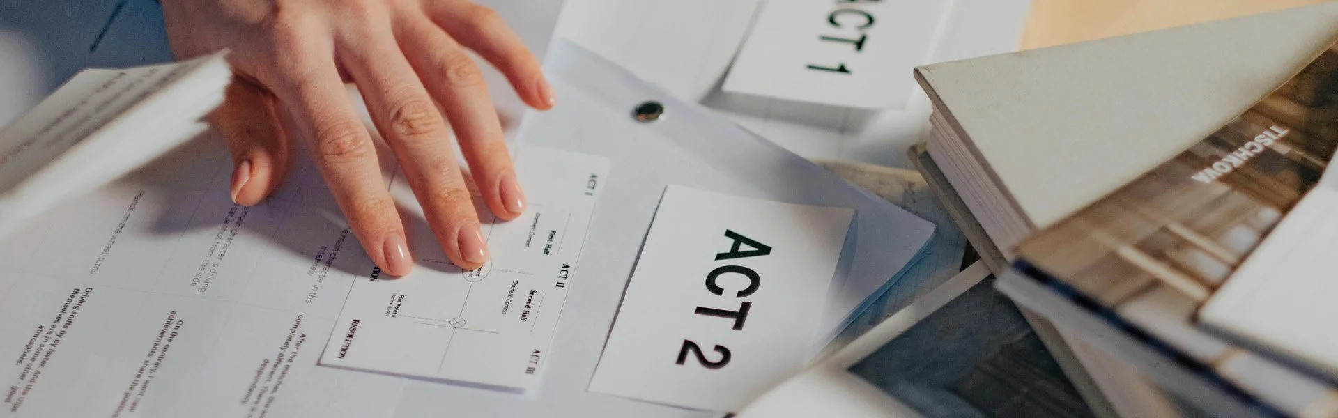 Hand organizing papers labeled Act 1 and Act 2 on a desk with books and documents
