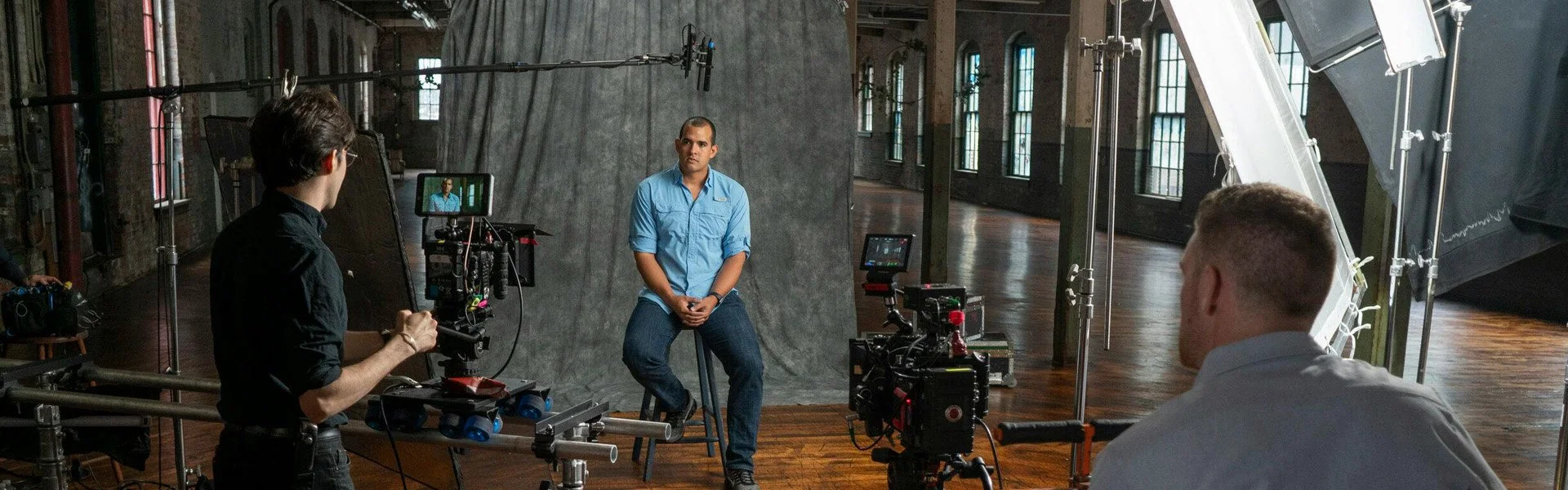 Man sitting for an interview with two camera operators and professional lighting equipment in a spacious indoor studio
