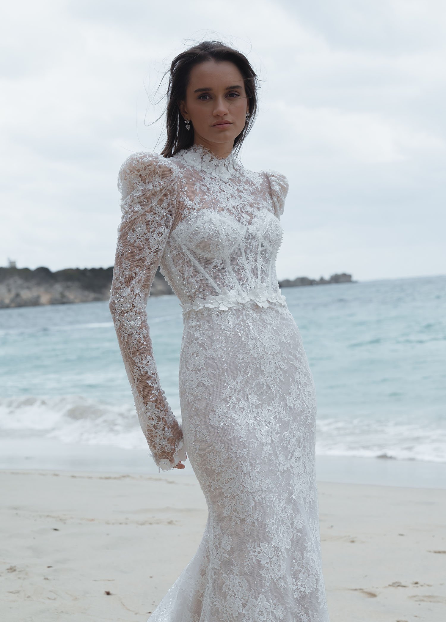 Jeune Austria-An innovative fit-and-flare wedding dress that redefines ocean-inspired elegance. This design strategically integrates lace and embellishments, anchored by a sophisticated, supportive high-neck bodice. A versatile floral accent adds a t