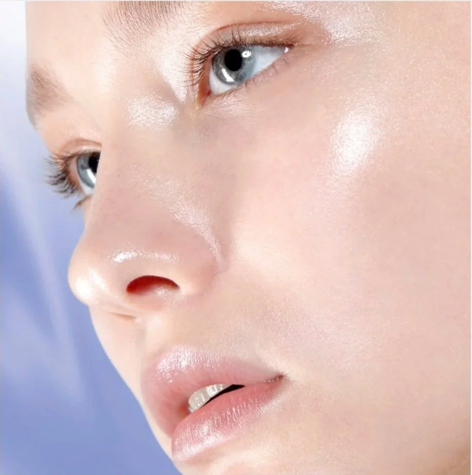Close-up of a woman's face with smooth, glowing skin, blue eyes, and light makeup.