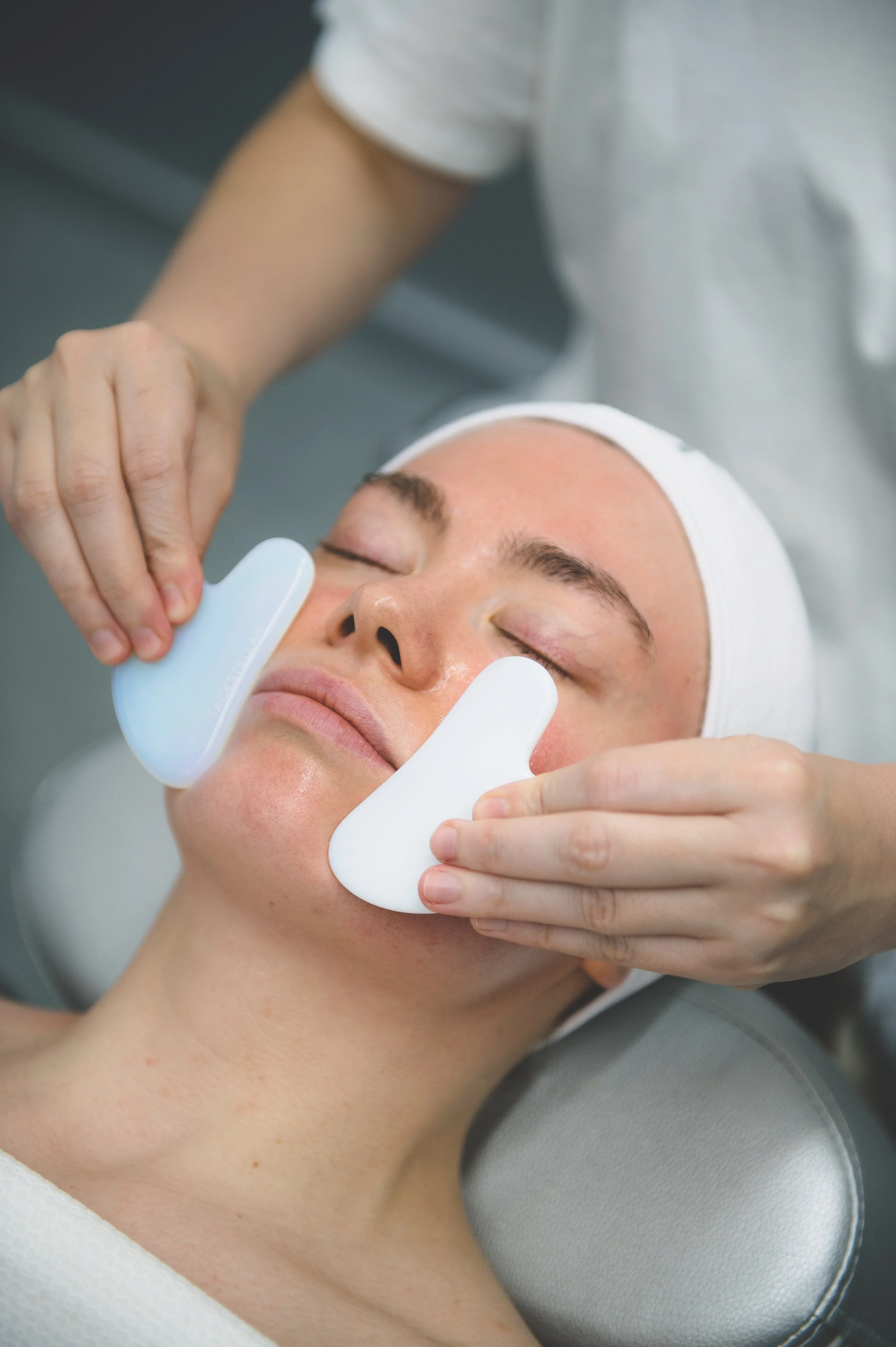A woman receiving a facial massage with guasha stones on her cheeks.