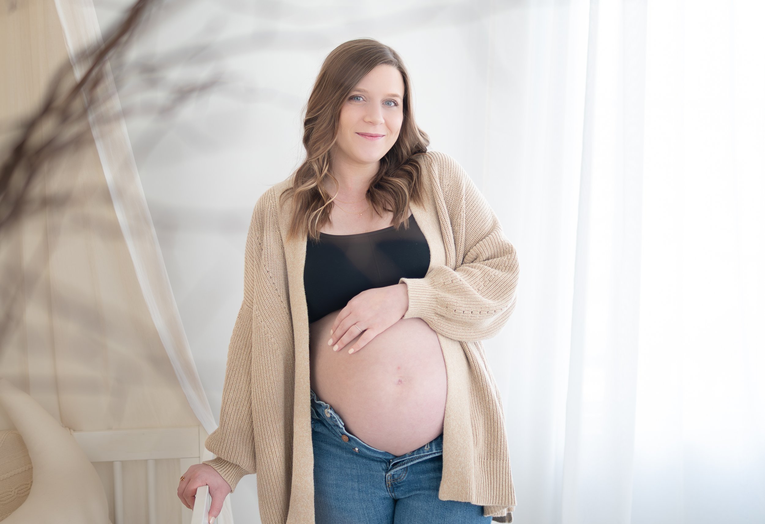 Pregnant woman in a beige cardigan, holding her belly.