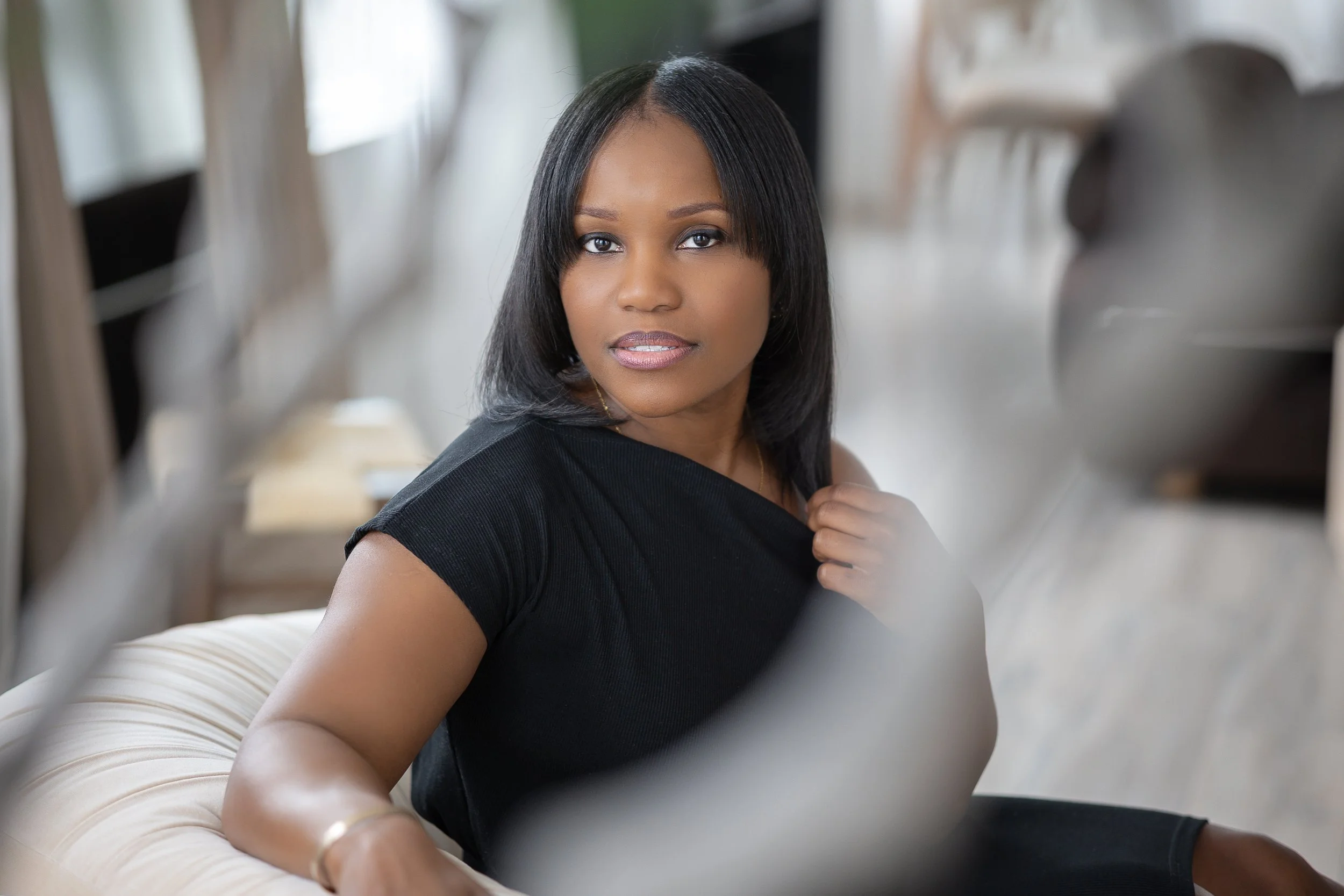 Woman seated on a sofa, wearing a black dress, looking at the camera.