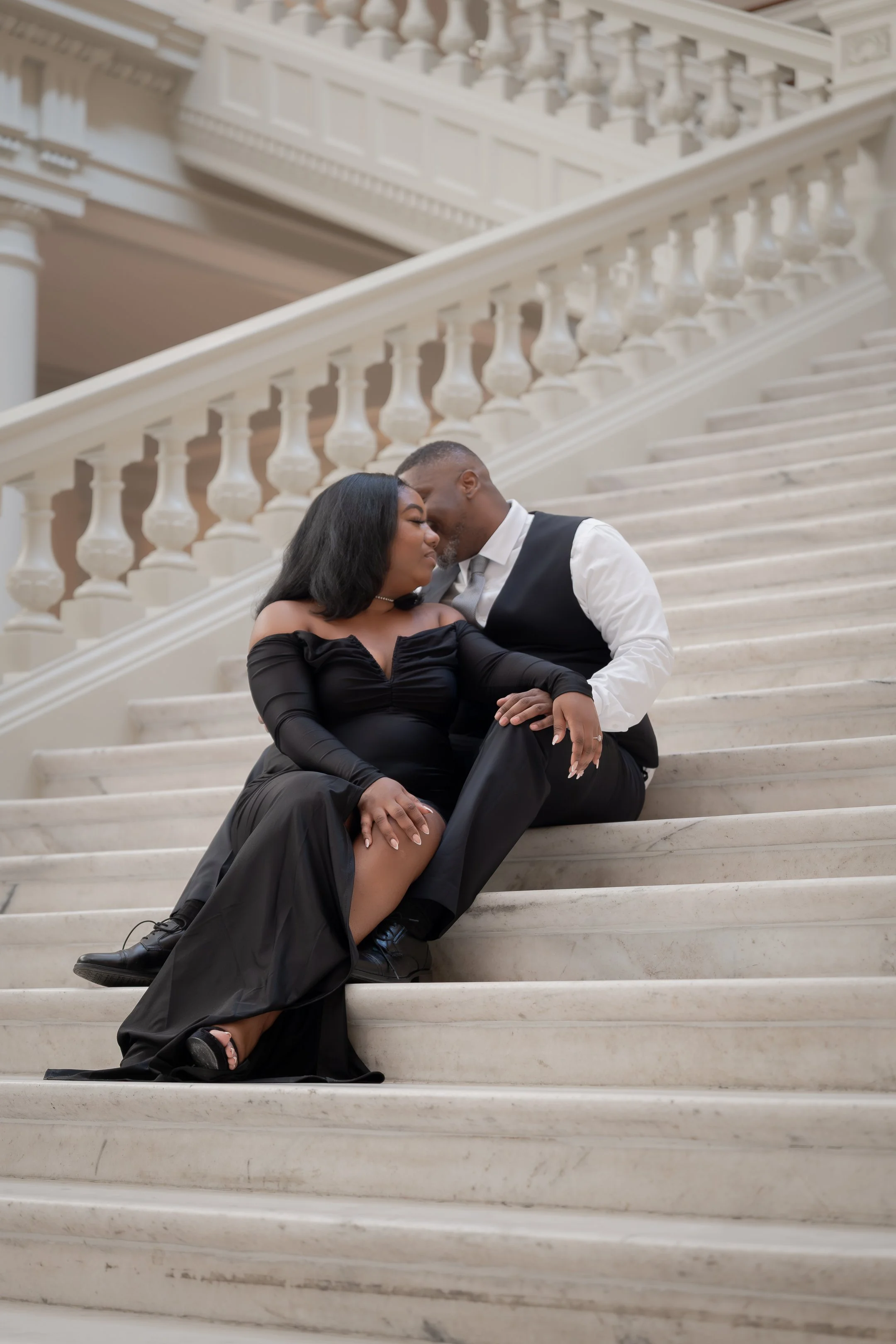 A couple sitting on marble stairs in an elegant building, embracing and touching foreheads.