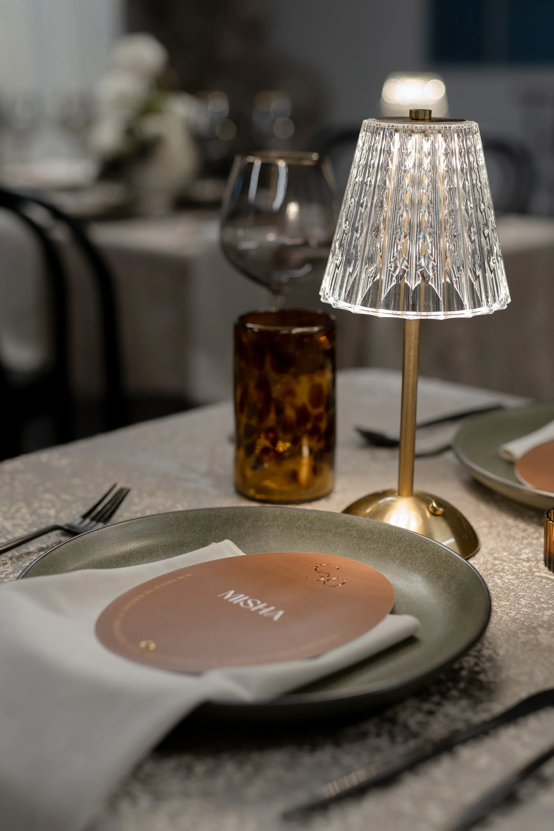 Elegant restaurant table setting with a decorative lamp, wine glass, plate, menu card, and cutlery.