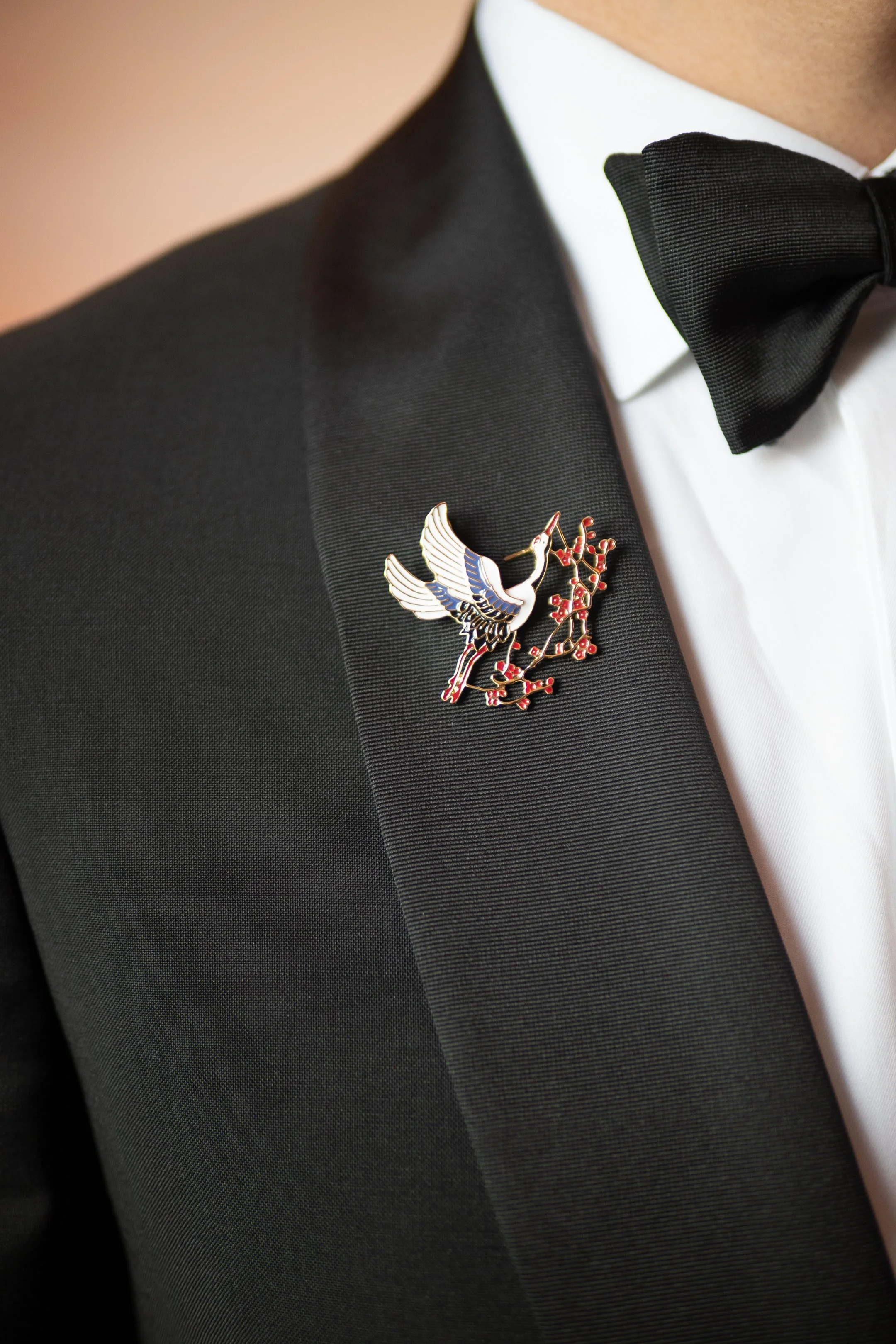 Close-up of a man in a tuxedo with a bird-shaped lapel pin and a bow tie.