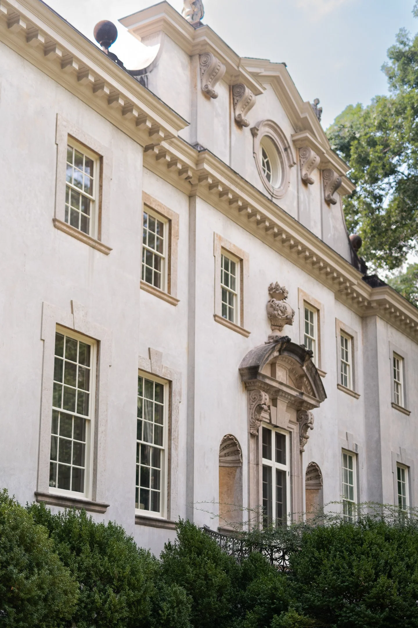 Elegant two-story classic building with ornate architectural details, large windows, and decorative stonework, surrounded by greenery.