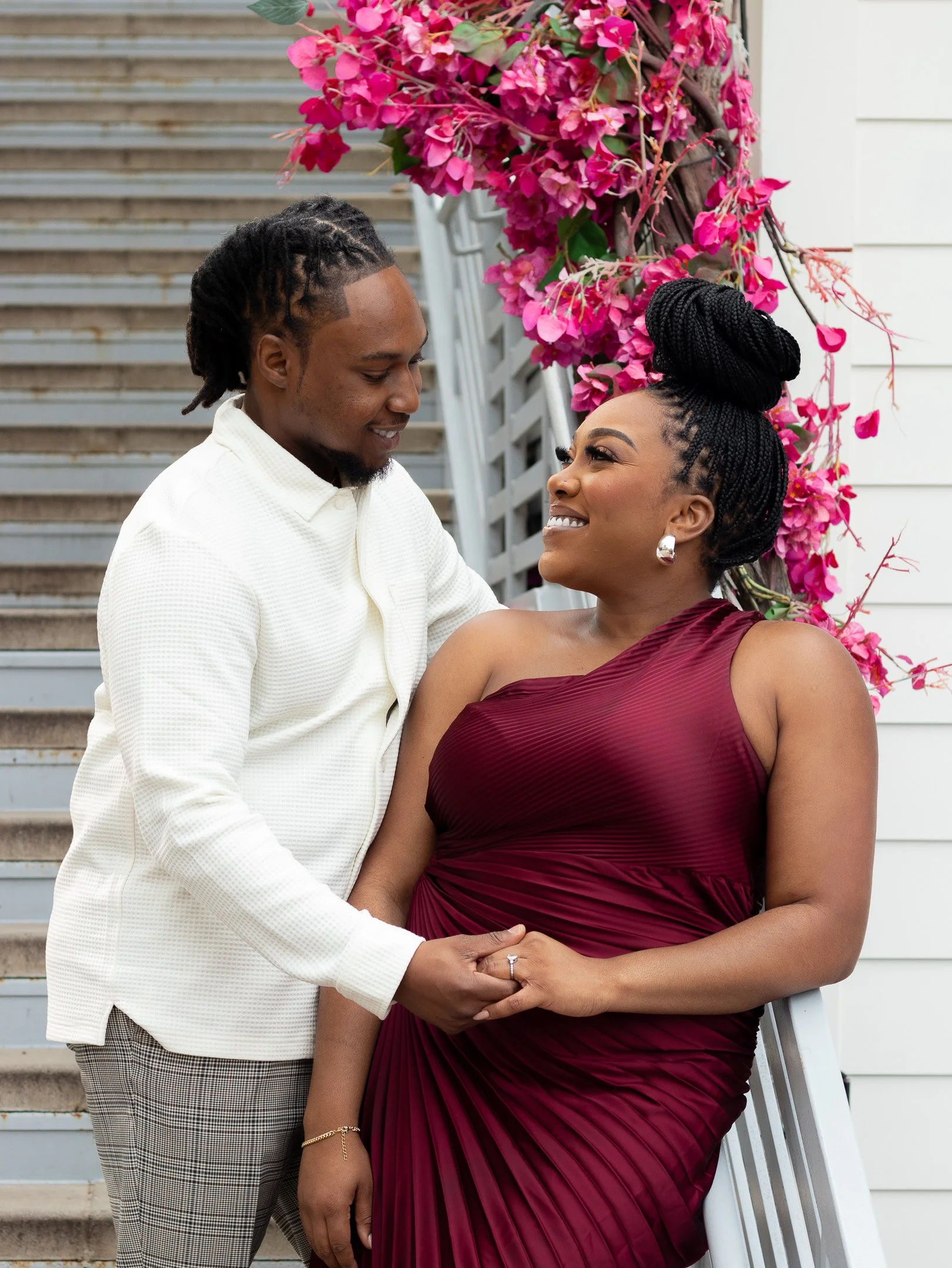 Couple affectionately holding hands on stairs with magenta flowers.