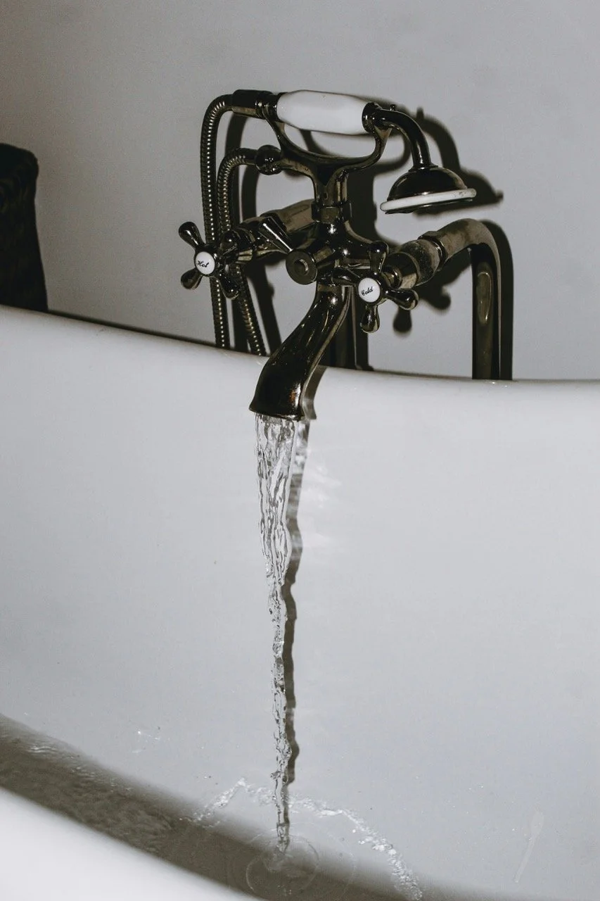 A running faucet with clear water flowing into a bathtub