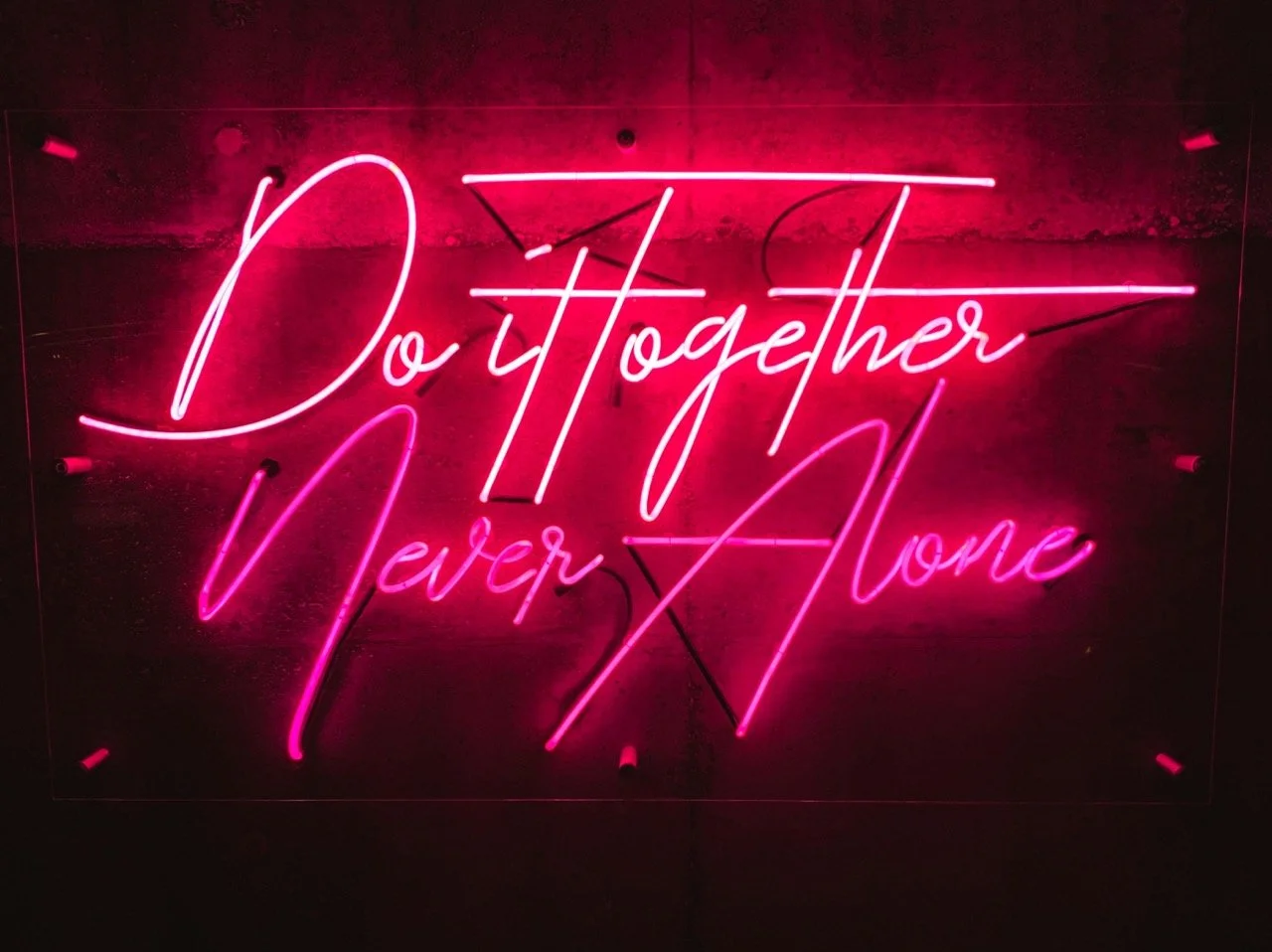 Pink and white neon sign that reads 'Do Together Never Alone' against a dark background.