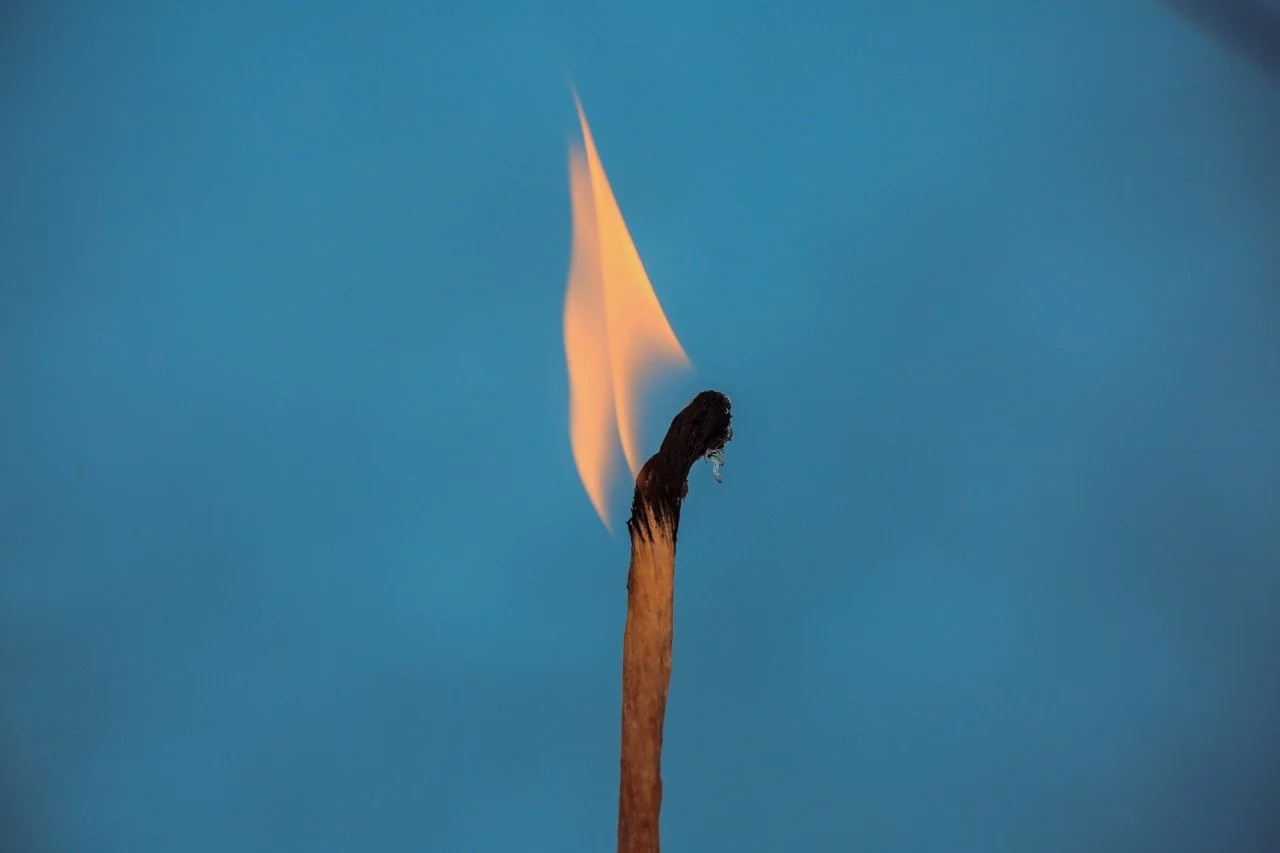 match burning in front of a dark blue sky