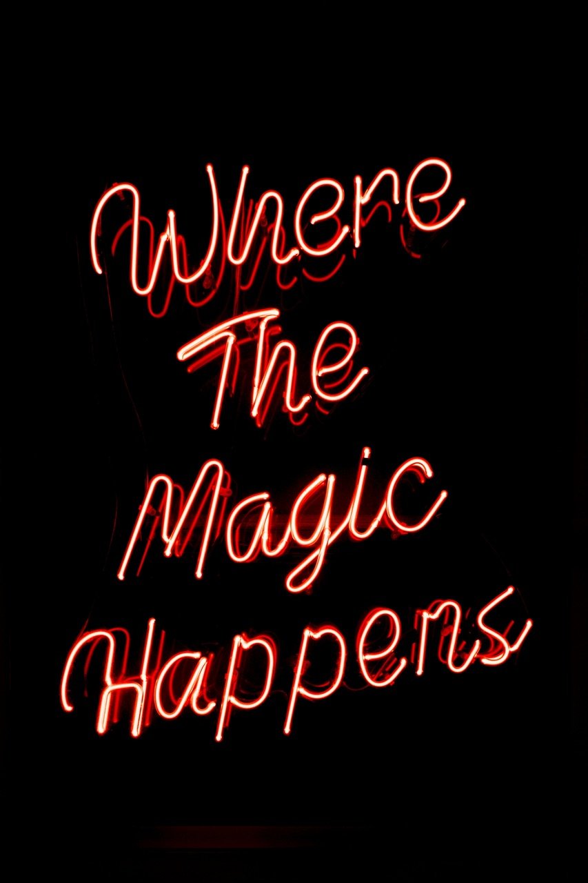 Red neon sign displaying the phrase 'Where The Magic Happens' on a black background.
