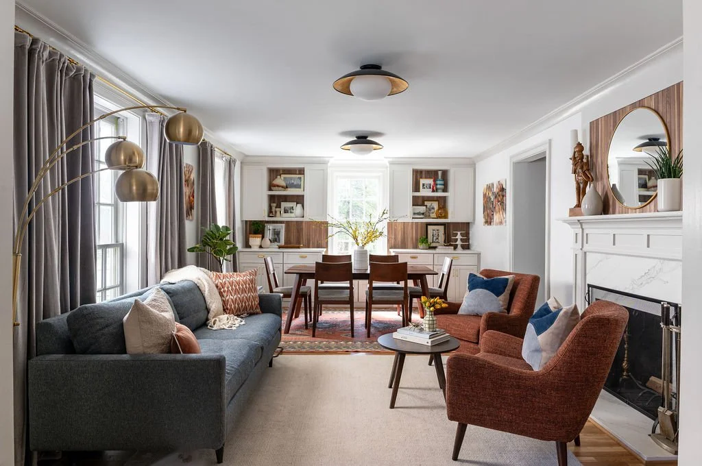 two copper colored chairs anchor the space in front of a fireplace. A walnut dining table sits in the background. Custom built in cabinets in Benjamin Moore Paint with walnut trim.