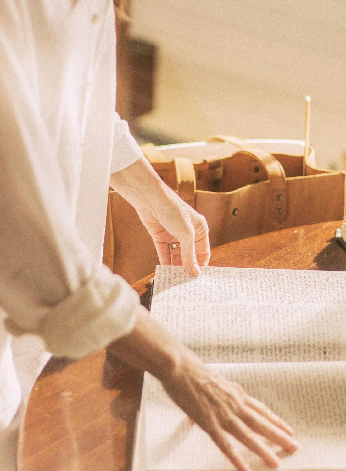 A person flipping through a newspaper or book at a wooden table, with a brown paper bag nearby.