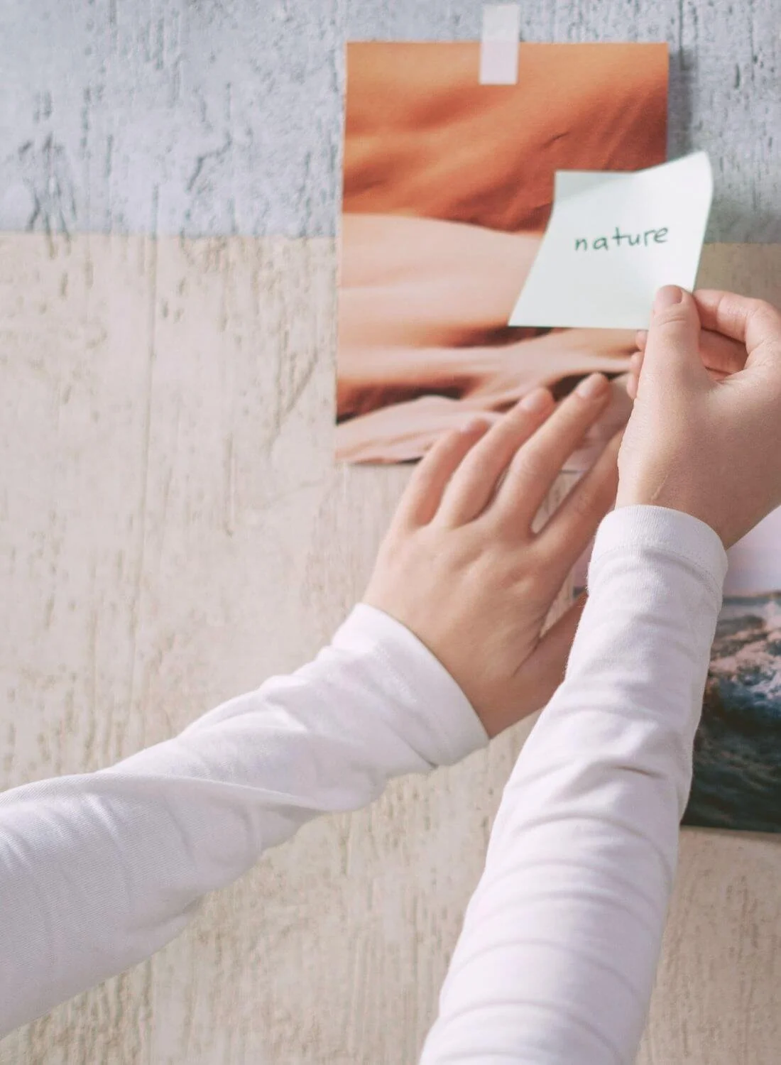 Person taping a note with the word 'nature' onto a photograph of a landscape with orange and pink tones.