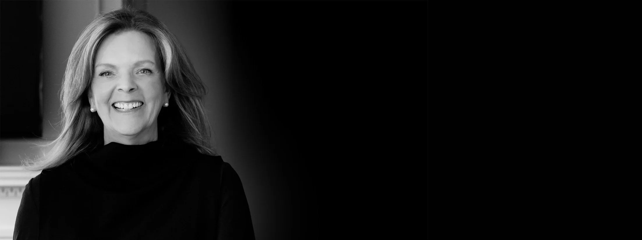 Susan Reid | Black and white portrait of a smiling with shoulder-length hair, wearing earrings and a dark top.