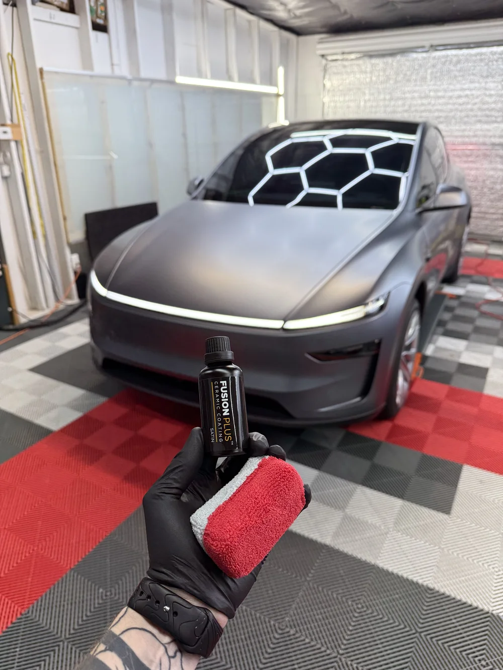 XPEL FUSION PLUS ceramic coating held beside a Tesla in the OCD installation bay