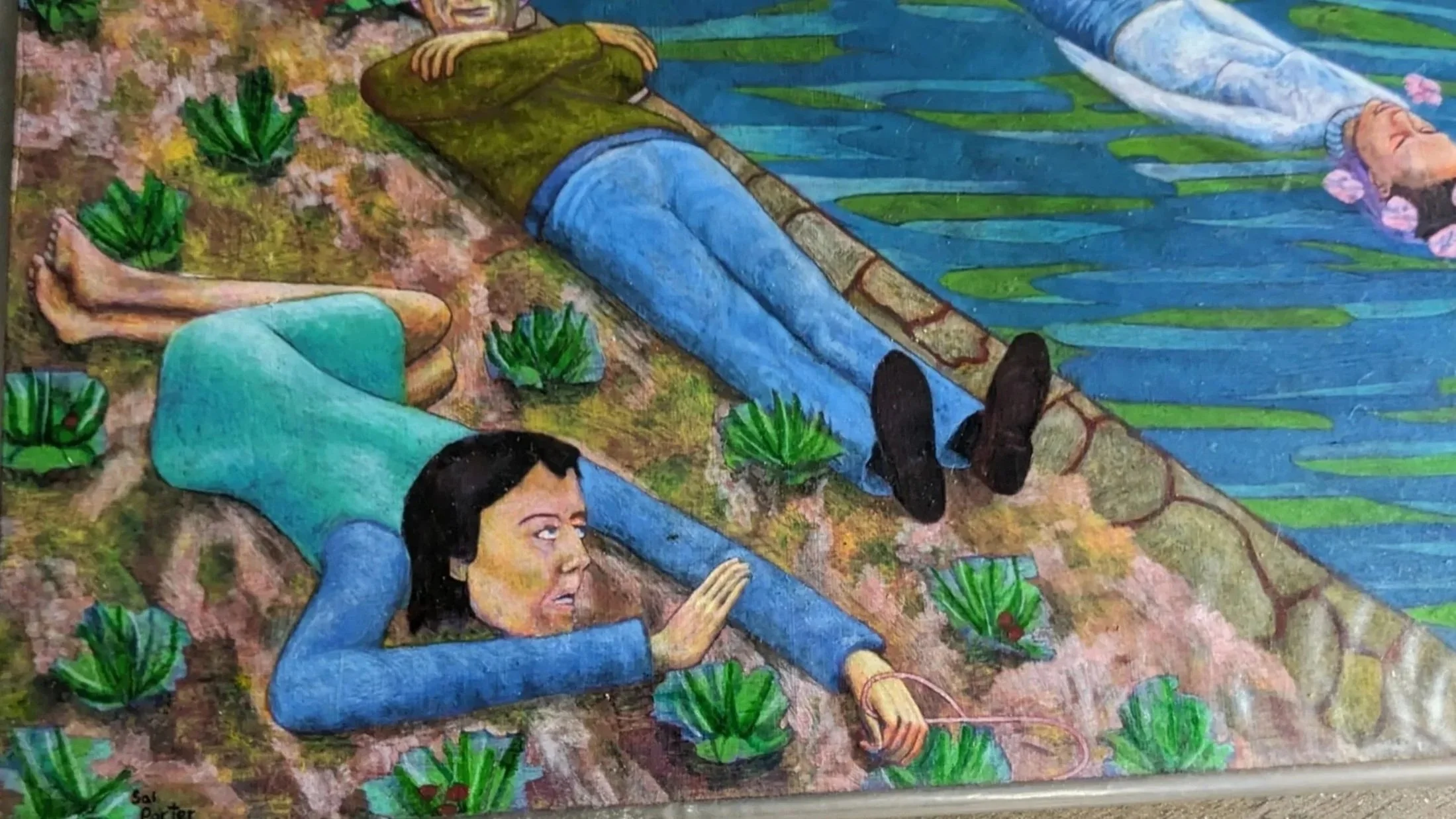 A colorful painting depicting two women lying on the ground near a water body. One woman is lying face down with an expression of concern, reaching out toward the water, while the other woman is floating in the water with her eyes closed and pink flowers around her head. Green plants surround them.